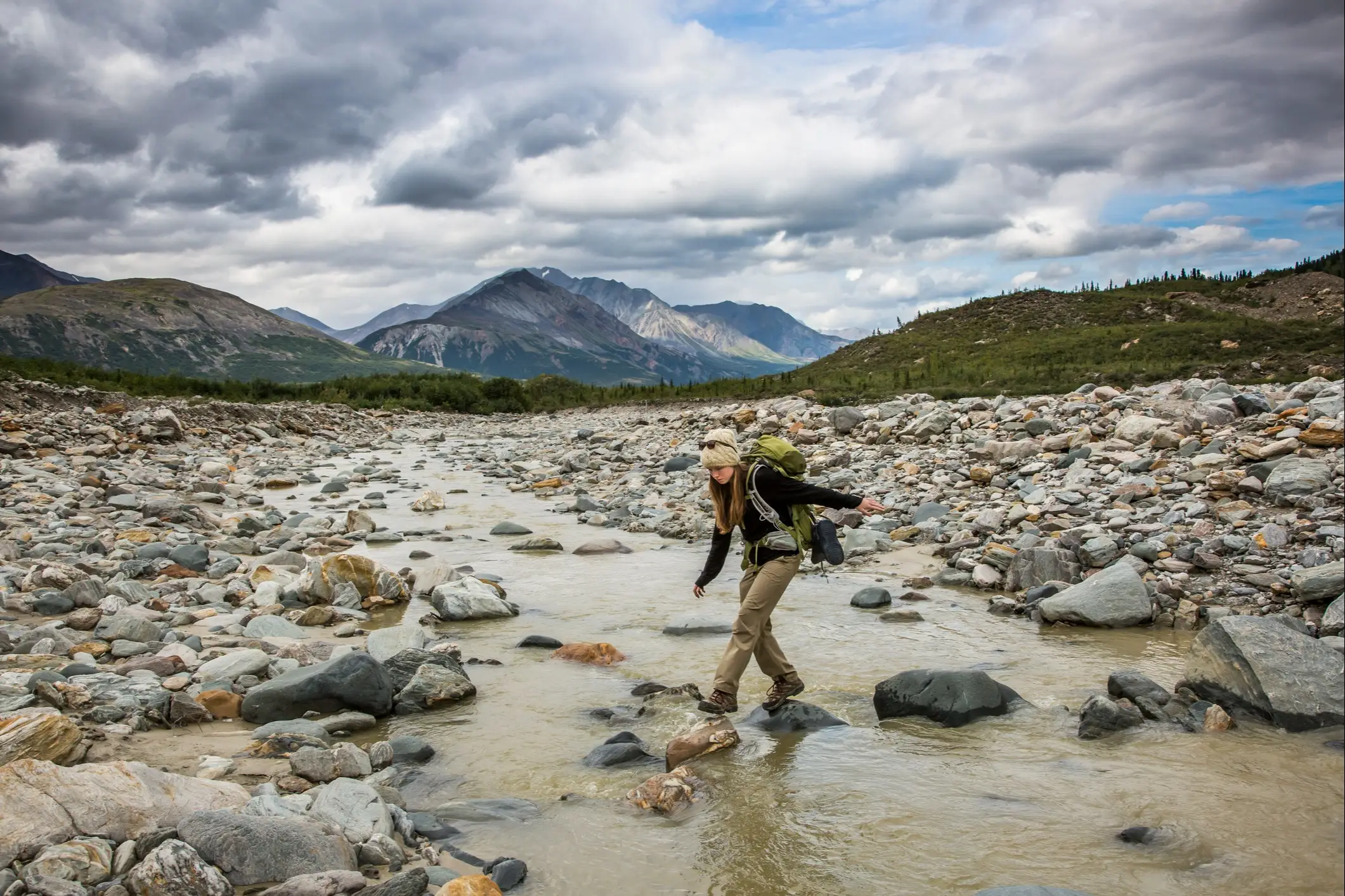 Alaska, Wandern Rucksacktouristin balanciert auf Felsen und überquert einen Fluss im Wildnisgebiet, Alaska.