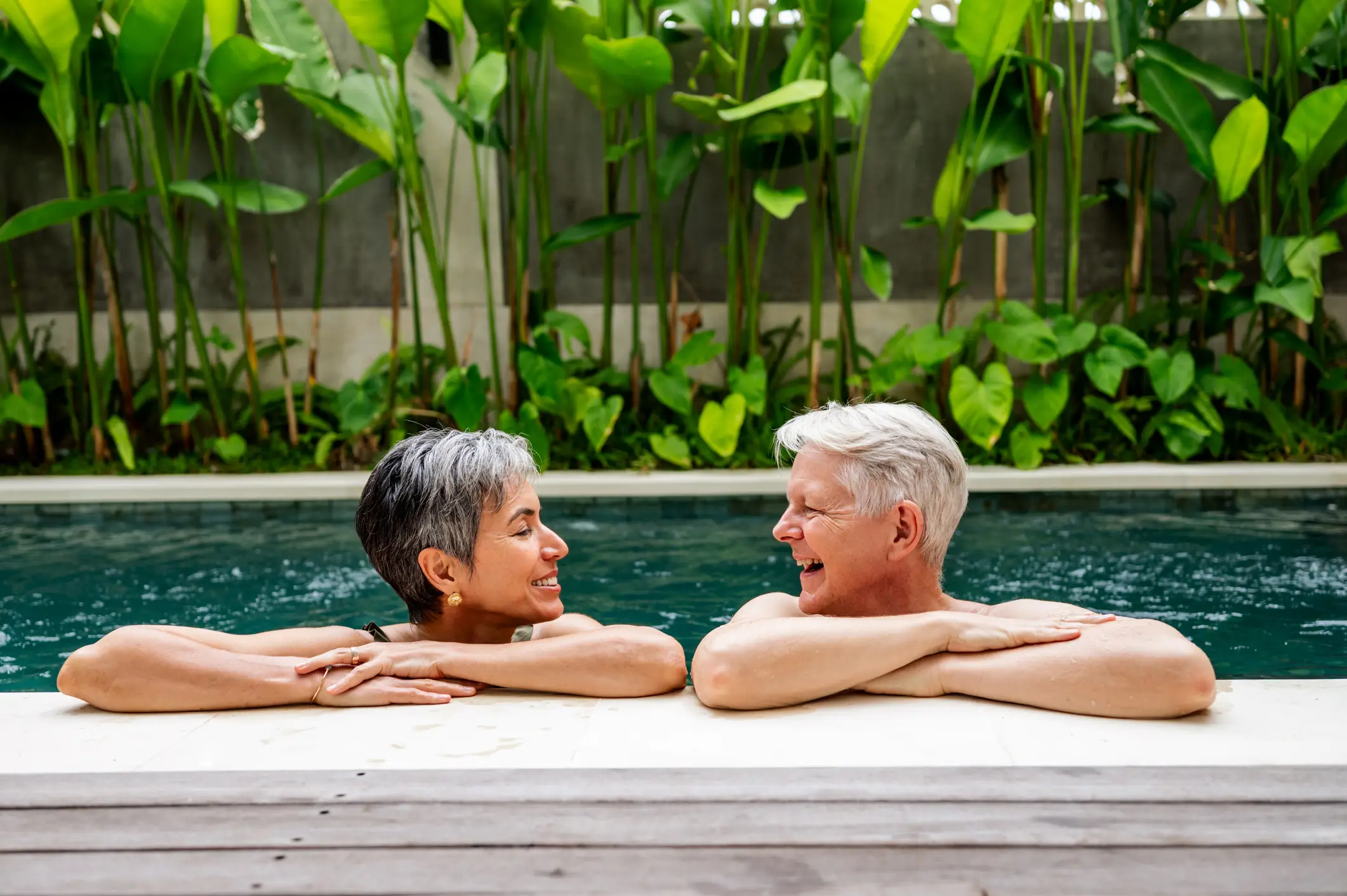 Indonesien, Spa Fröhliches Seniorenpaar, das Gespräche und Entspannung am Pool in einem üppigen tropischen Garten genießt