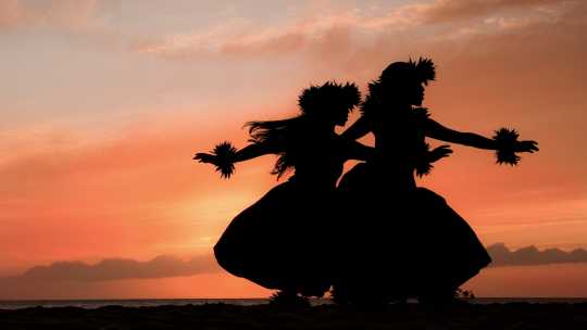 Zwei hawaiianische Hula-Tänzerinnen bewegen sich anmutig vor dem warmen Schein des tropischen Sonnenuntergangs auf Hawaii, USA.