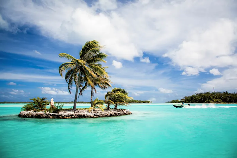 Petit motu avec palmiers et une eau turquoise, avec un bateau, Bora Bora, Polynésie Française.