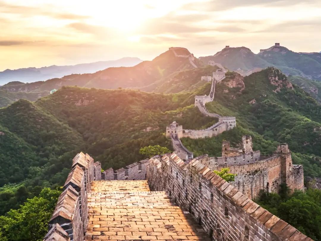 Historische Chinesische Mauer mit Sonnenuntergang und Bergen im Hintergrund. Peking, China.