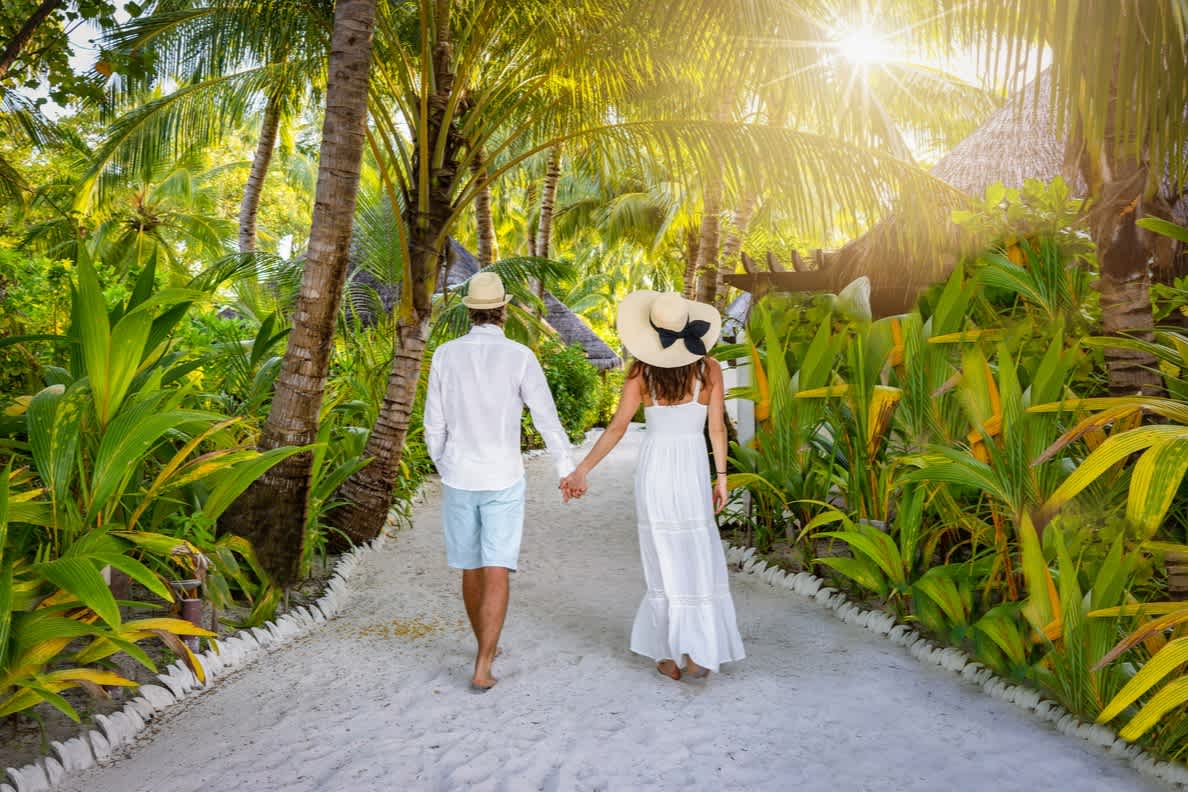 Paar hält sich an den Händen auf einem von tropischen Pflanzen bewachsenen Weg