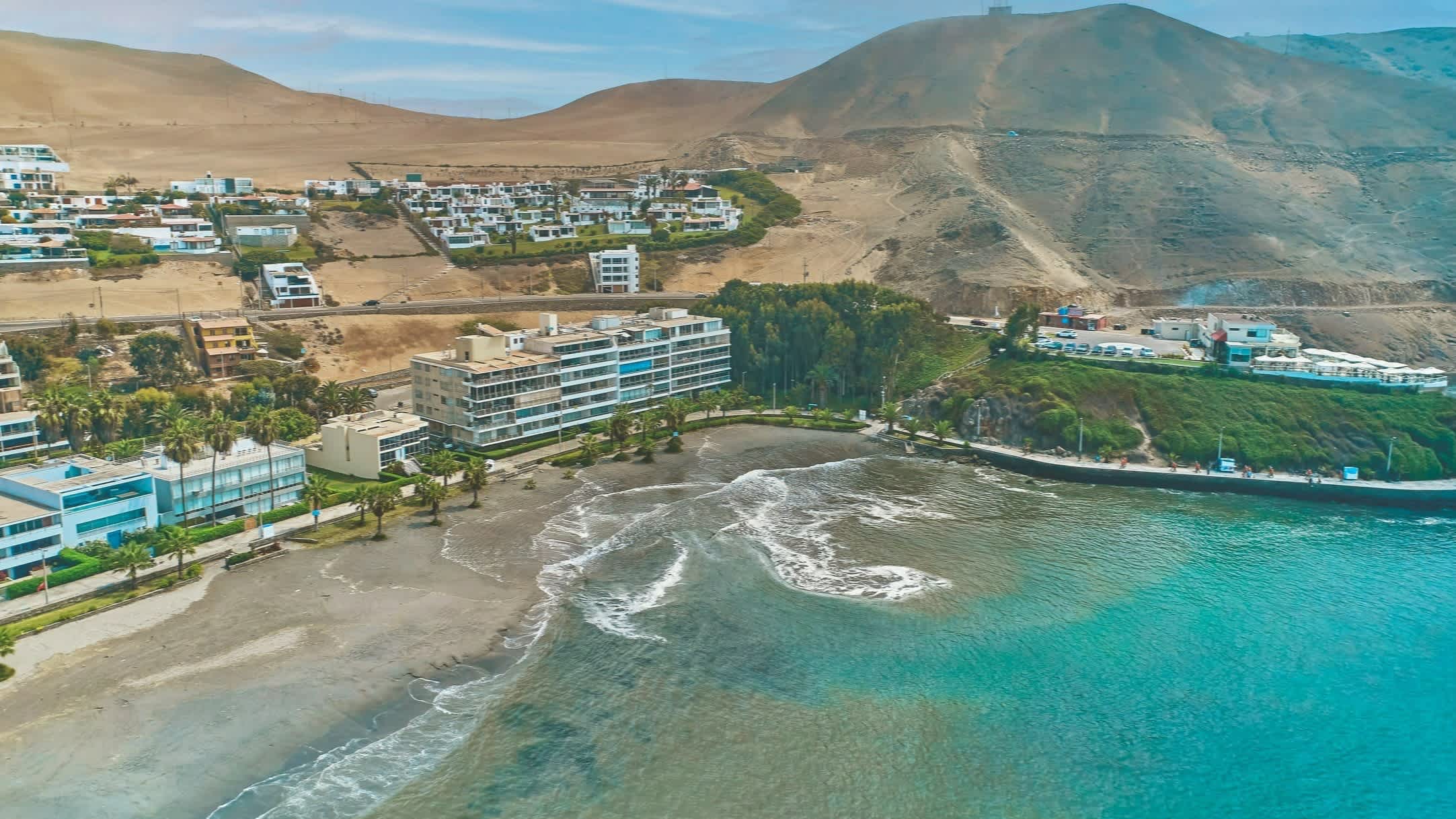Drohnenaufnahme von der Bucht Ancon, Peru bei sonnigem Wetter und mit Blick auf das blaue Meer und Hotels an der Promenade.