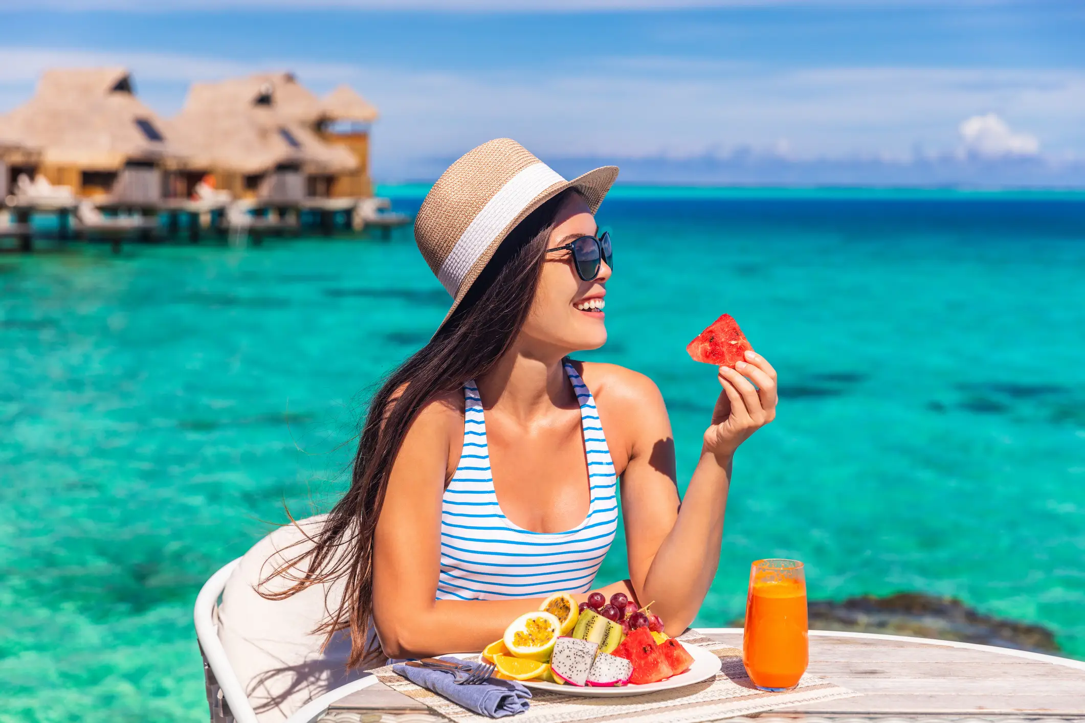 Femme savourant des fruits tropicaux avec vue sur les eaux turquoises et les bungalows sur pilotis, Bora bora, Polynésie française.