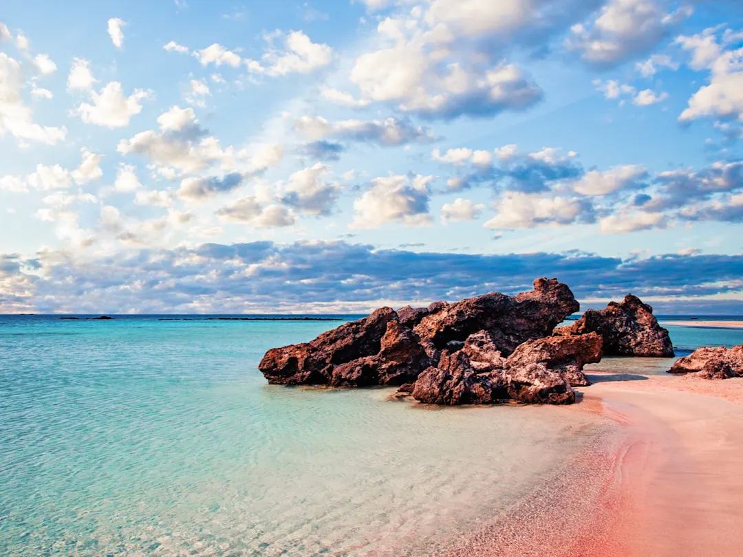 Der Elafonissi Strand auf Kreta besticht durch sein kristallklares, türkisfarbenes Wasser und den rosafarbenen Sand, der durch Muscheln und Korallen entsteht