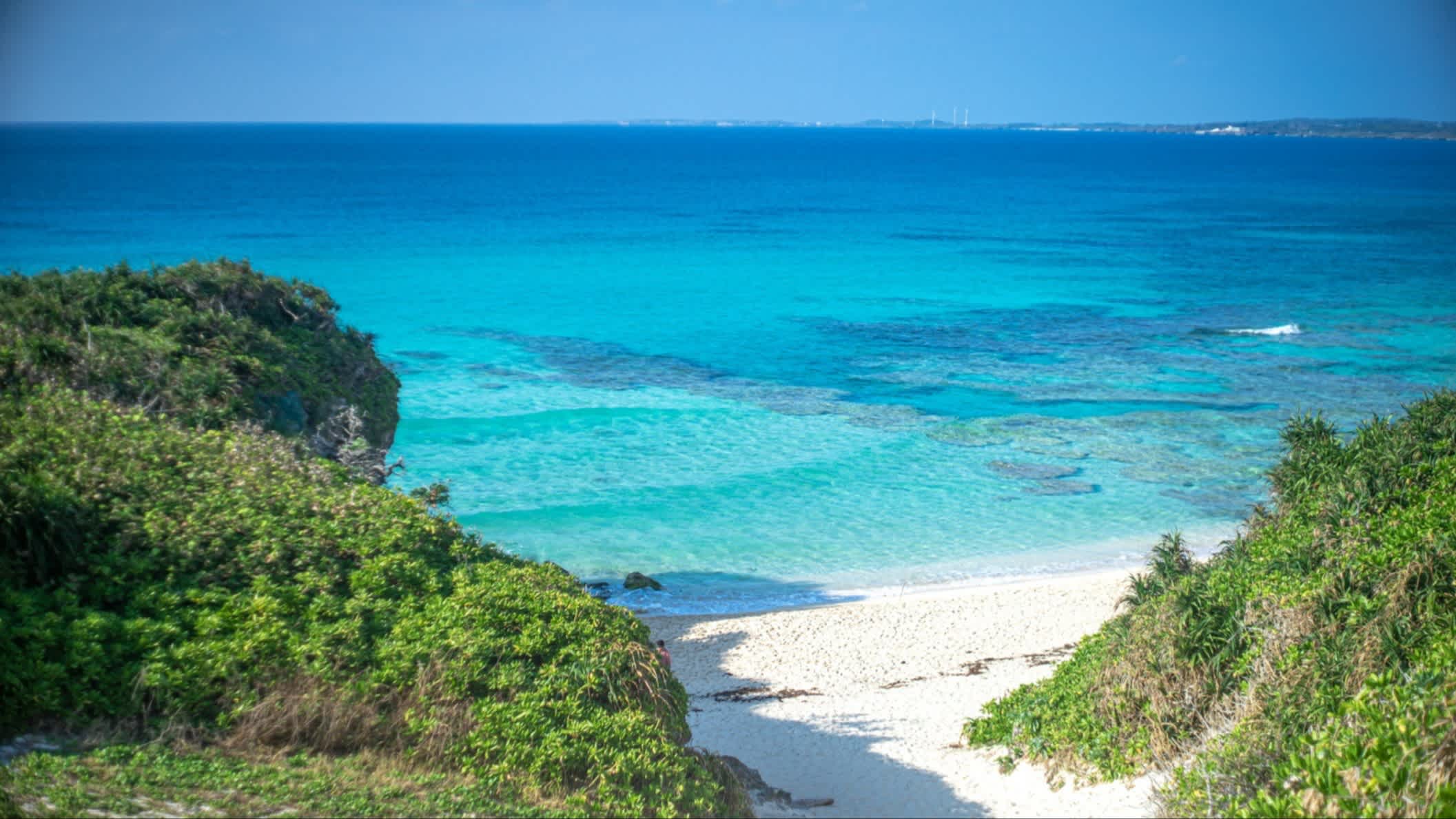 Weißer Sandstrand von Sunayama, Okinawa, Japan am blauen Meer, mit weißem Sand und grünen Hügeln.