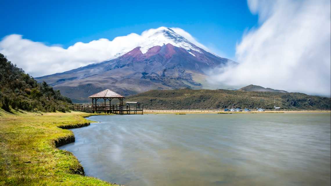 Vue panoramique sur le volcan Cotopaxi et un pavillon en bois sur pilotis au pied du volcan, Équateur.