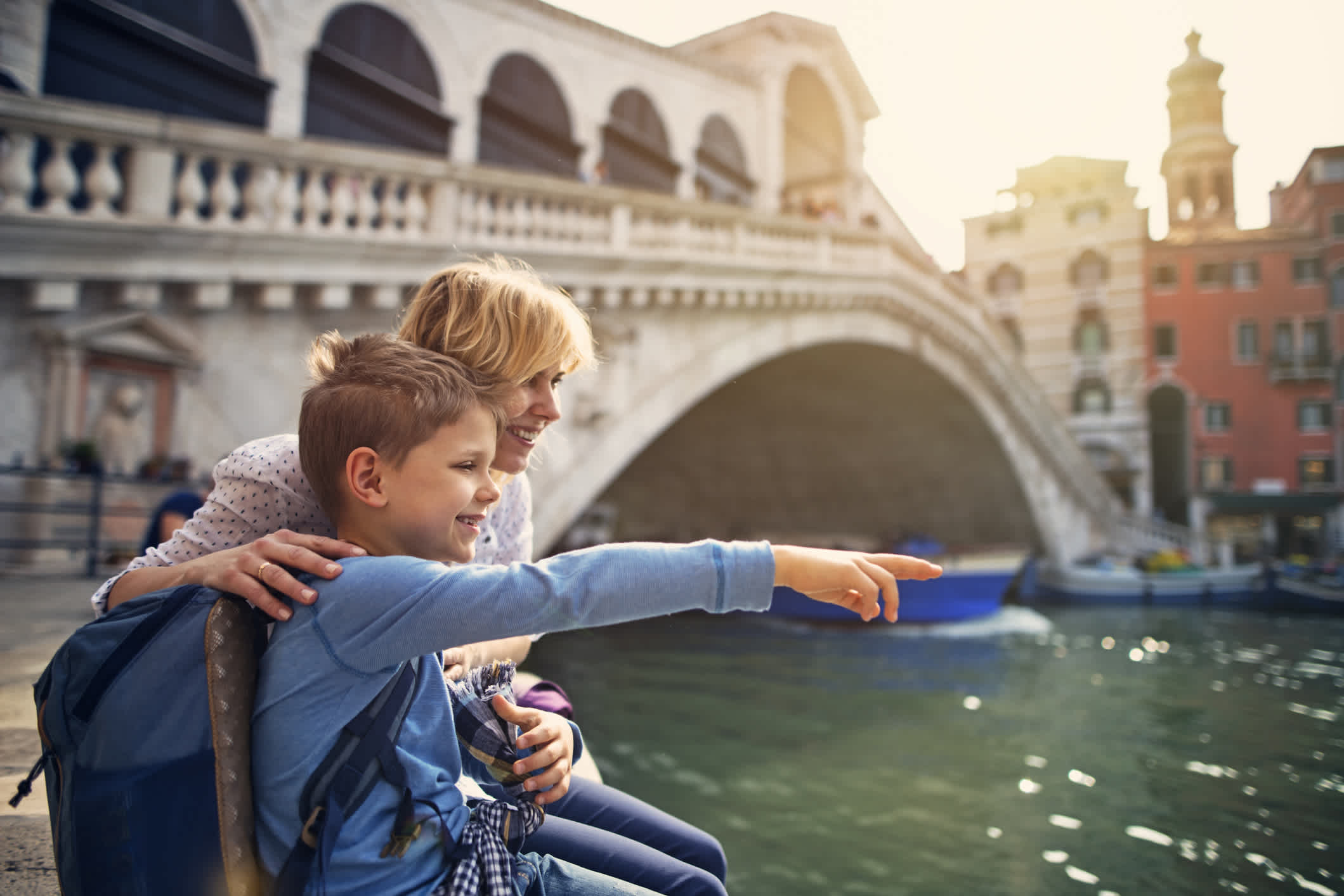Mutter und Sohn besuchen Venedig, Italien. Sie sitzen am großen Kanal und die berühmte Rialto-Brücke ist im Hintergrund zu sehen.