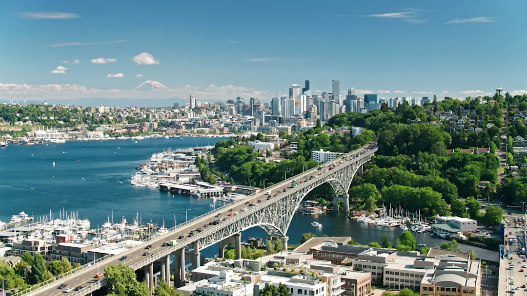 Luftaufnahme von Seattle, Washington an einem sonnigen Tag im Sommer, Blick entlang der Aurora Bridge vom Fremont-Ufer des Lake Union in Richtung East Queen Anne und Eastlake, mit der Skyline der Innenstadt in der Ferne und, viel weiter entfernt, der Schneekappe des Mount Rainier.