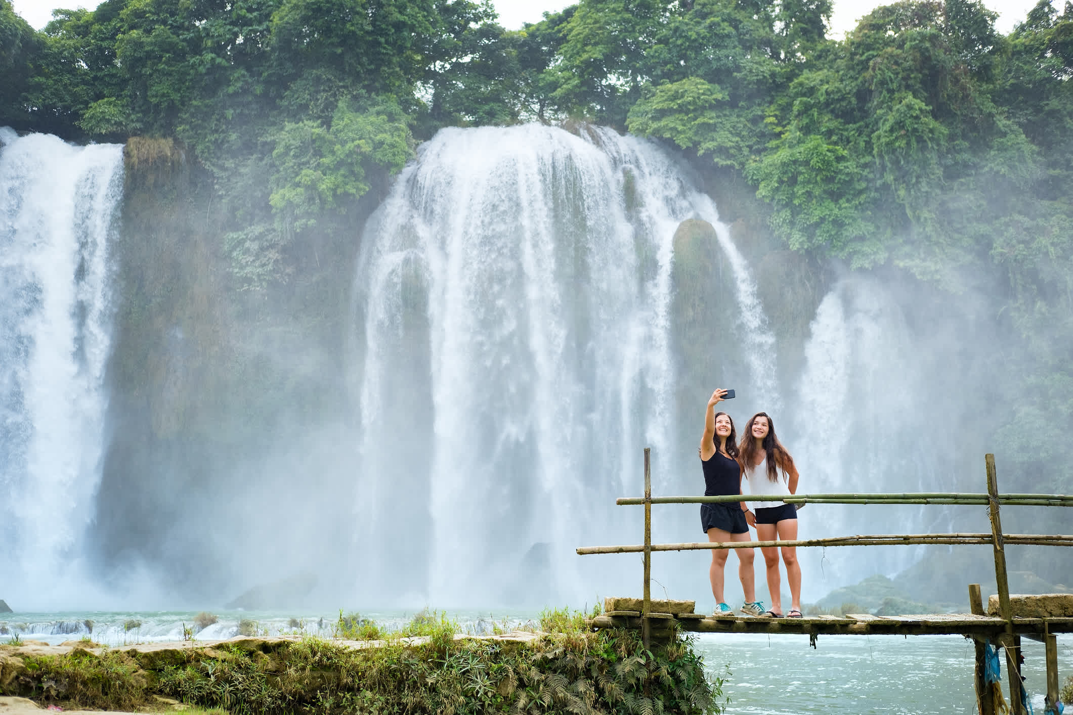 De jeunes voyageurs se tiennent sur un pont, avec les chutes de Ban Gioc en arrière-plan, dans la province de Cao Bang, au nord du Vietnam.