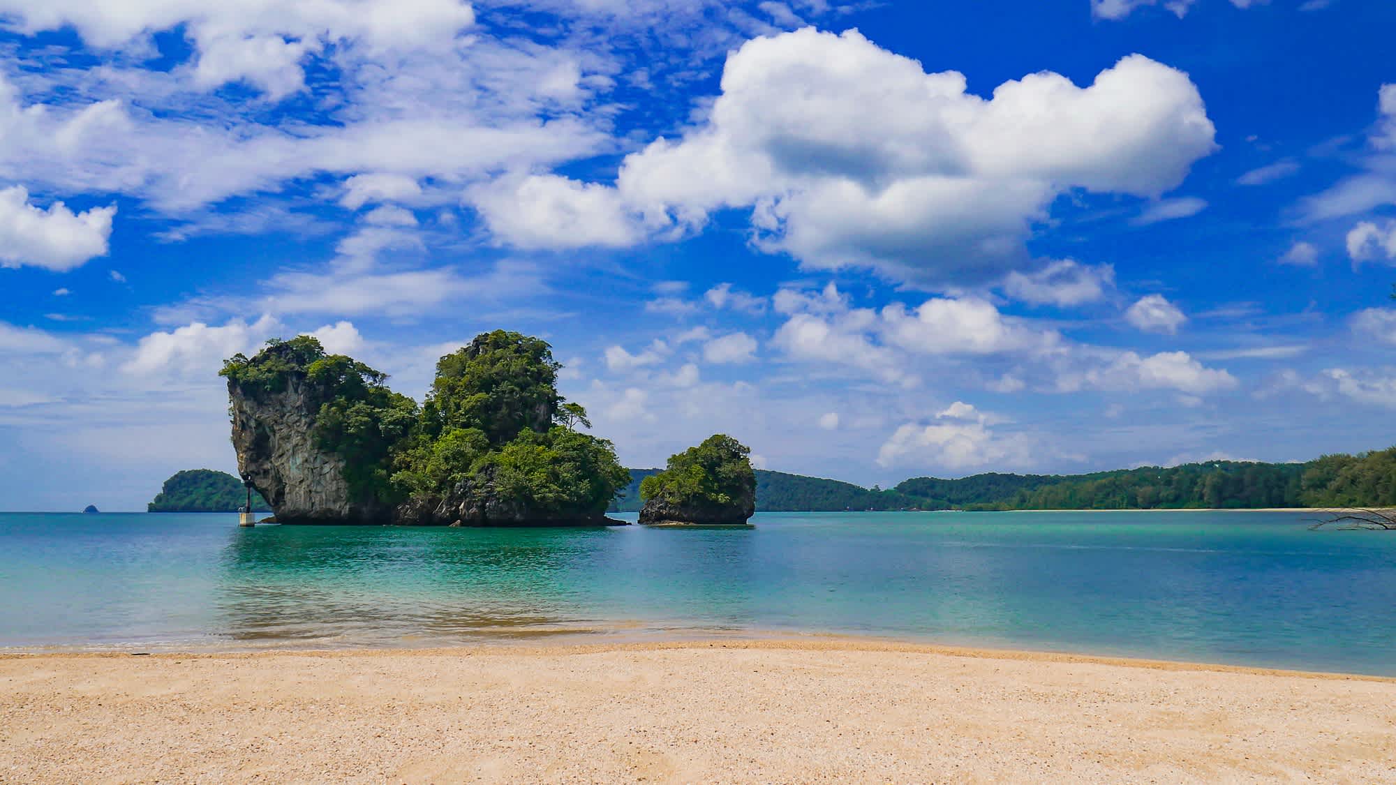 Vue des rochers recouvert de végétation depuis le sable blanc au bord de l'eau turquoise de la plage de Nopparat Thara en Thaïlande