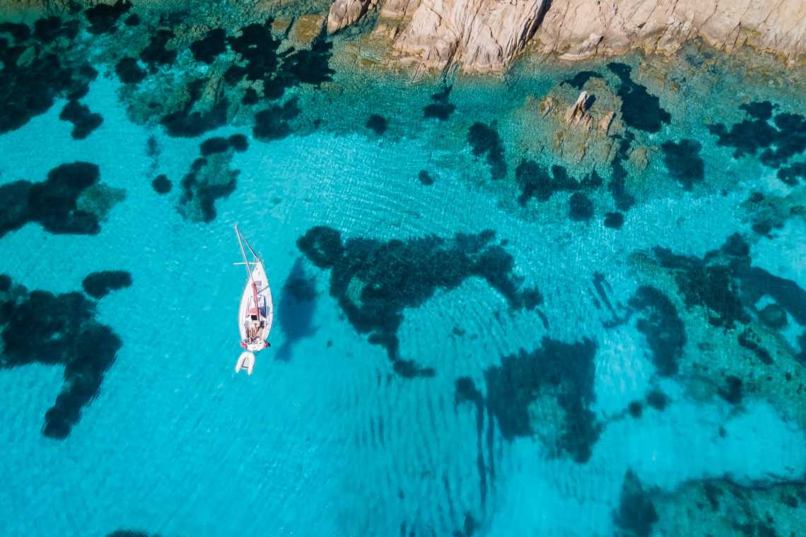 Blick von oben, atemberaubende Luftaufnahme eines Segelbootes, das auf einem türkisfarbenen und transparenten Wasser segelt. Sardinien, Italien