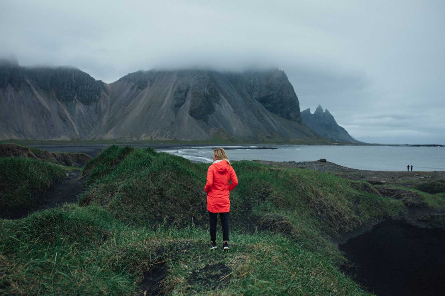 Voyagez avec Tourlane, femme au manteau rouge faisant face à la mer.