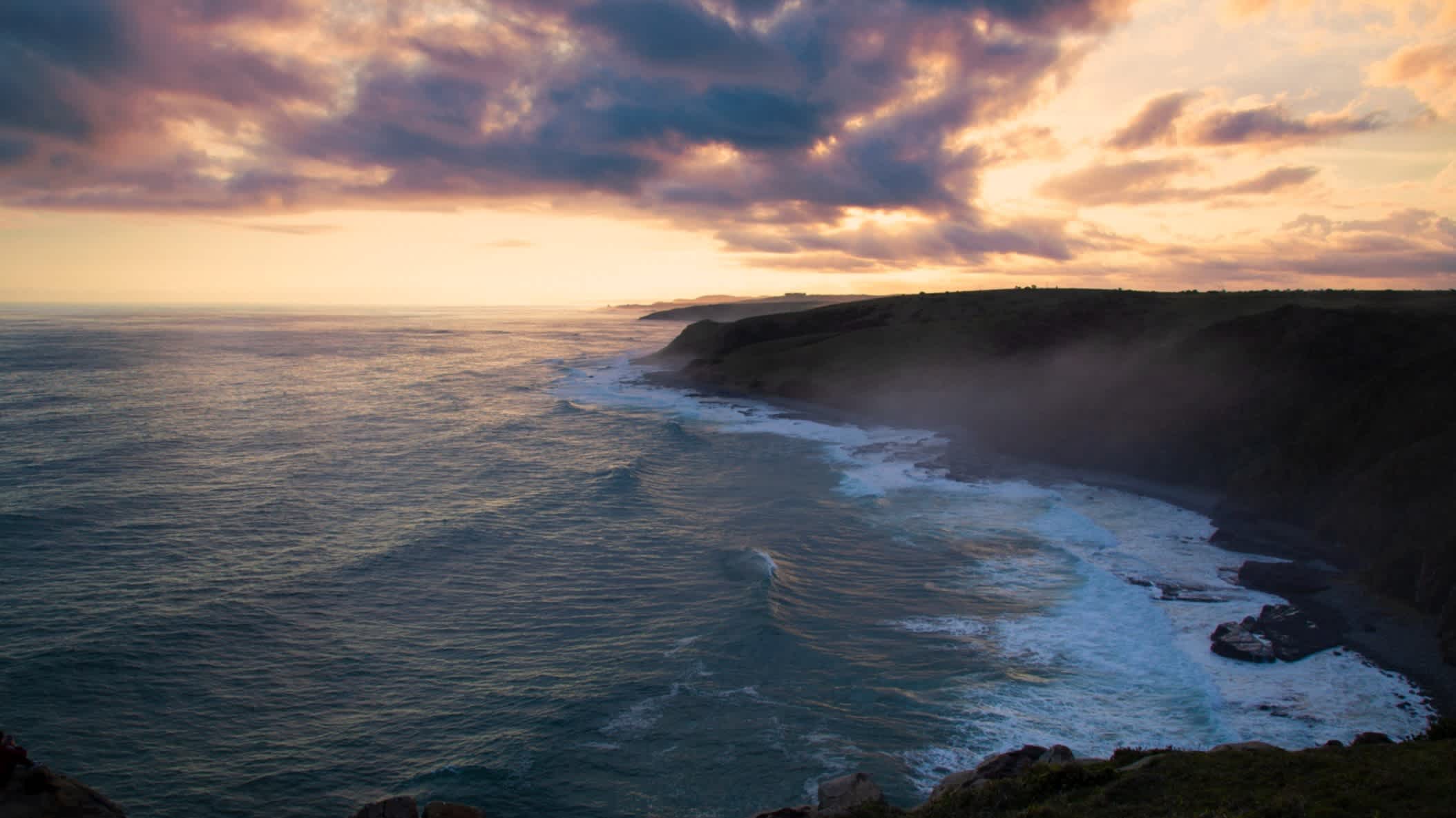 Die Klippen der Morgan Bay bei gedimmtem Sonnenlicht und Wolken am Himmel mit Aussicht auf das Meer an der wilden Eastern Cape Küste Südafrikas. 