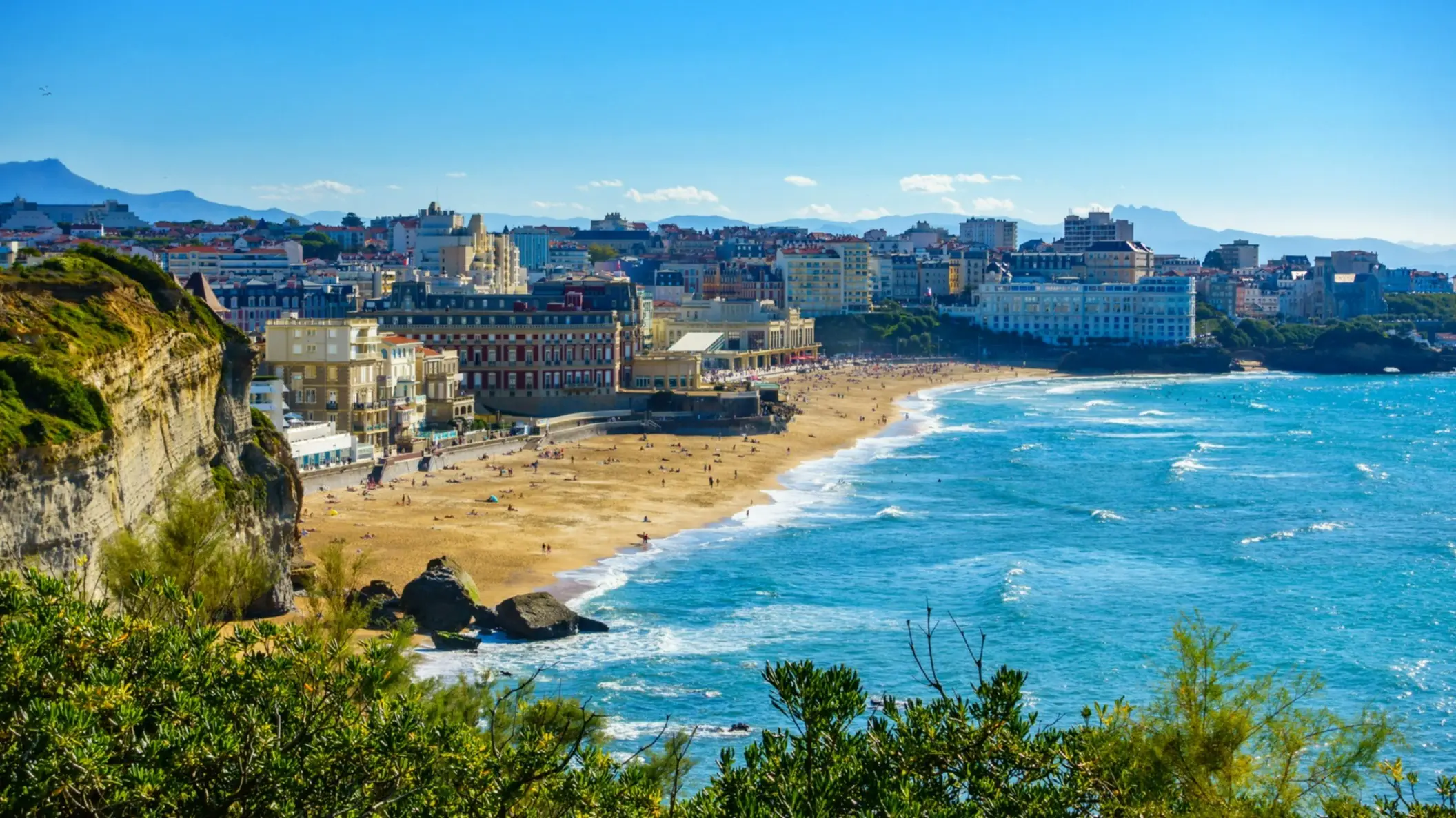 Die Bucht von Biarritz Grande Plage in Frankreich mit Aussicht von einem Viewpoint und Blick auf die Stadt sowie das Meer bei blauem Himmel.

