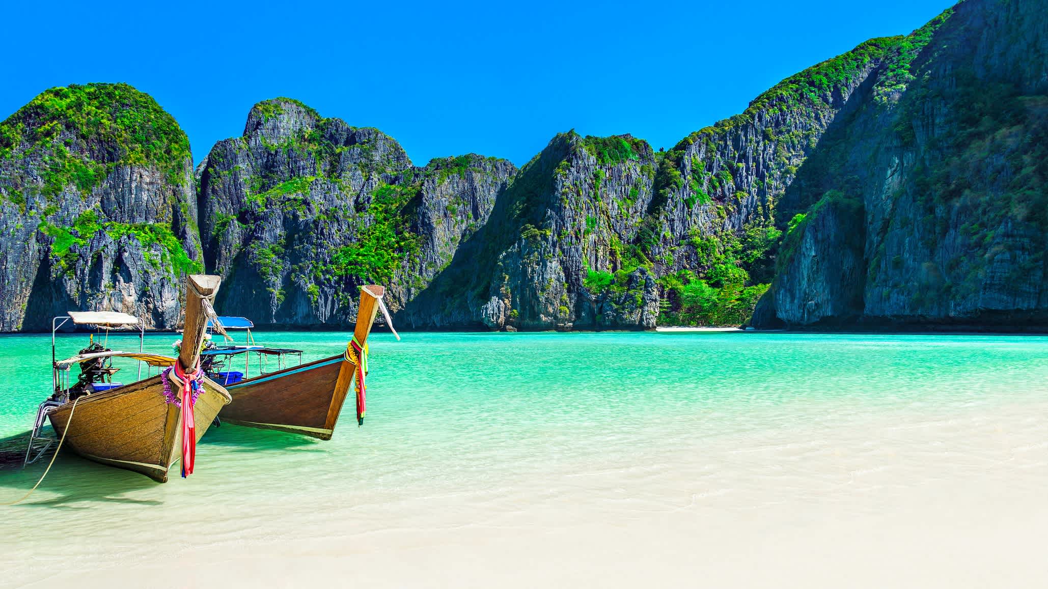 Célèbre plage pittoresque de Maya Bay sur l'île de Ko Phi Phi Leh en Thaïlande avec deux bateaux-taxis traditionnels à longue queue et des collines calcaires abruptes en arrière-plan.