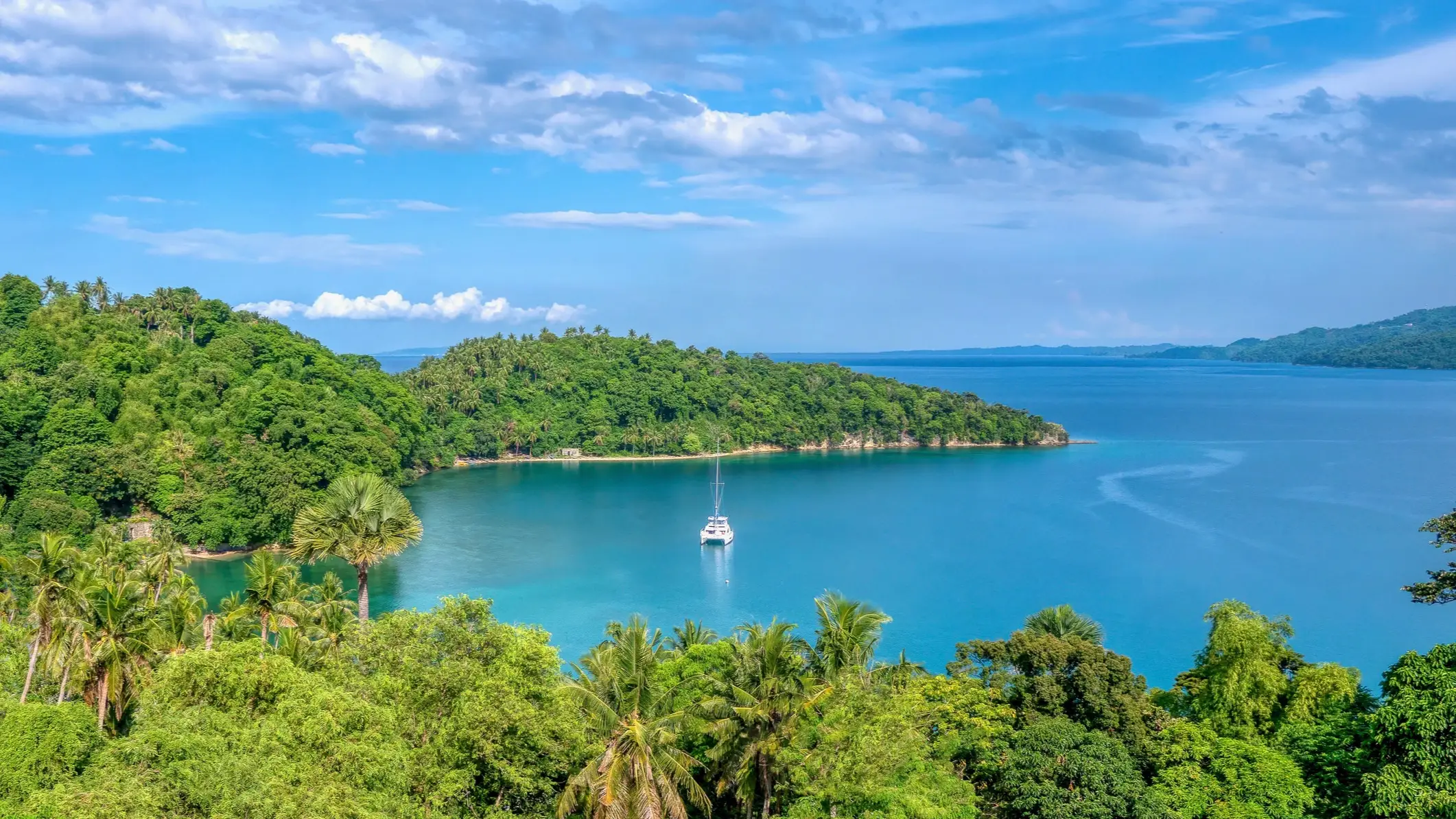 Mindoro, Mimaropa, Philippinen Grüne tropische Insel mit Bucht und Segelboot im blauen Wasser, Mindoro, Mimaropa, Philippinen.