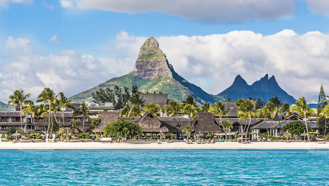 Strandresort mit Palmen vor Bergkulisse und klarem Wasser. Flic-en-Flac, Rivière Noire, Mauritius