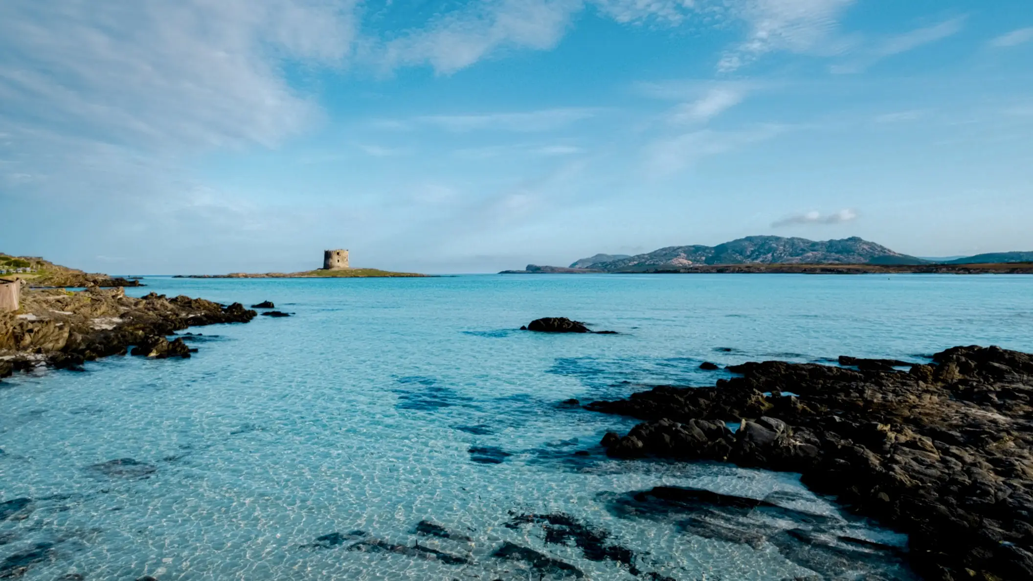 Blick vom Strand La Pelosa, Sardinien, Italien auf das Meer mit einer vorgelagerten Insel sowie einer Festung.