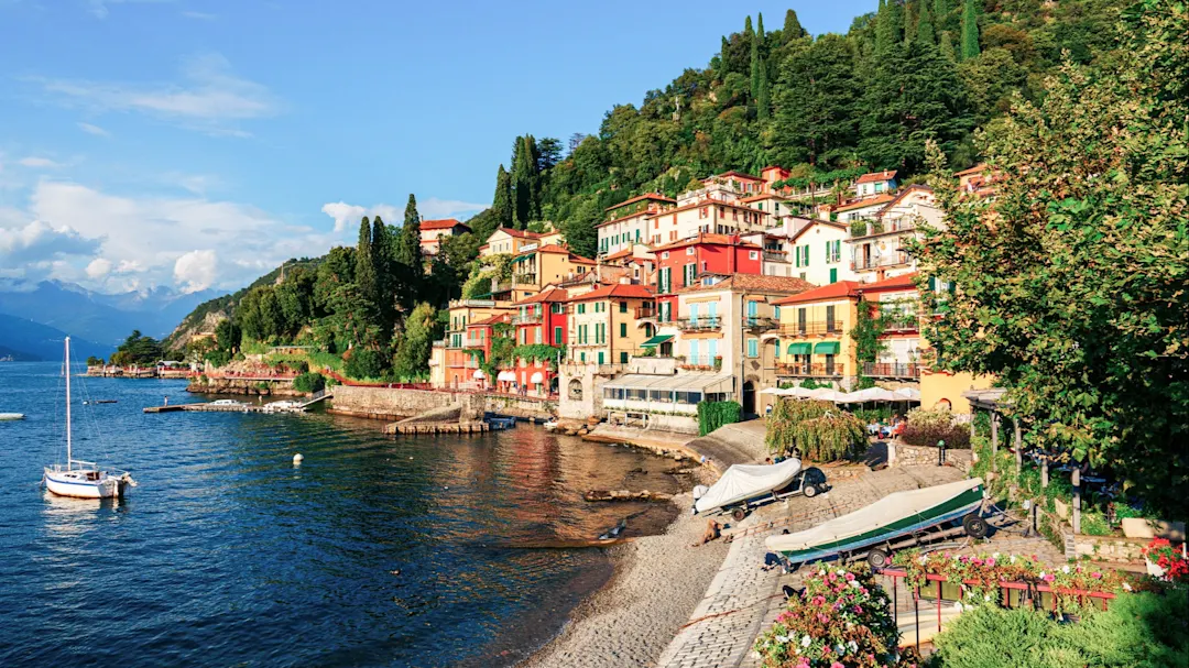 Bunte Häuser am Ufer eines Sees mit Hügeln im Hintergrund. Varenna, Comer See, Italien.