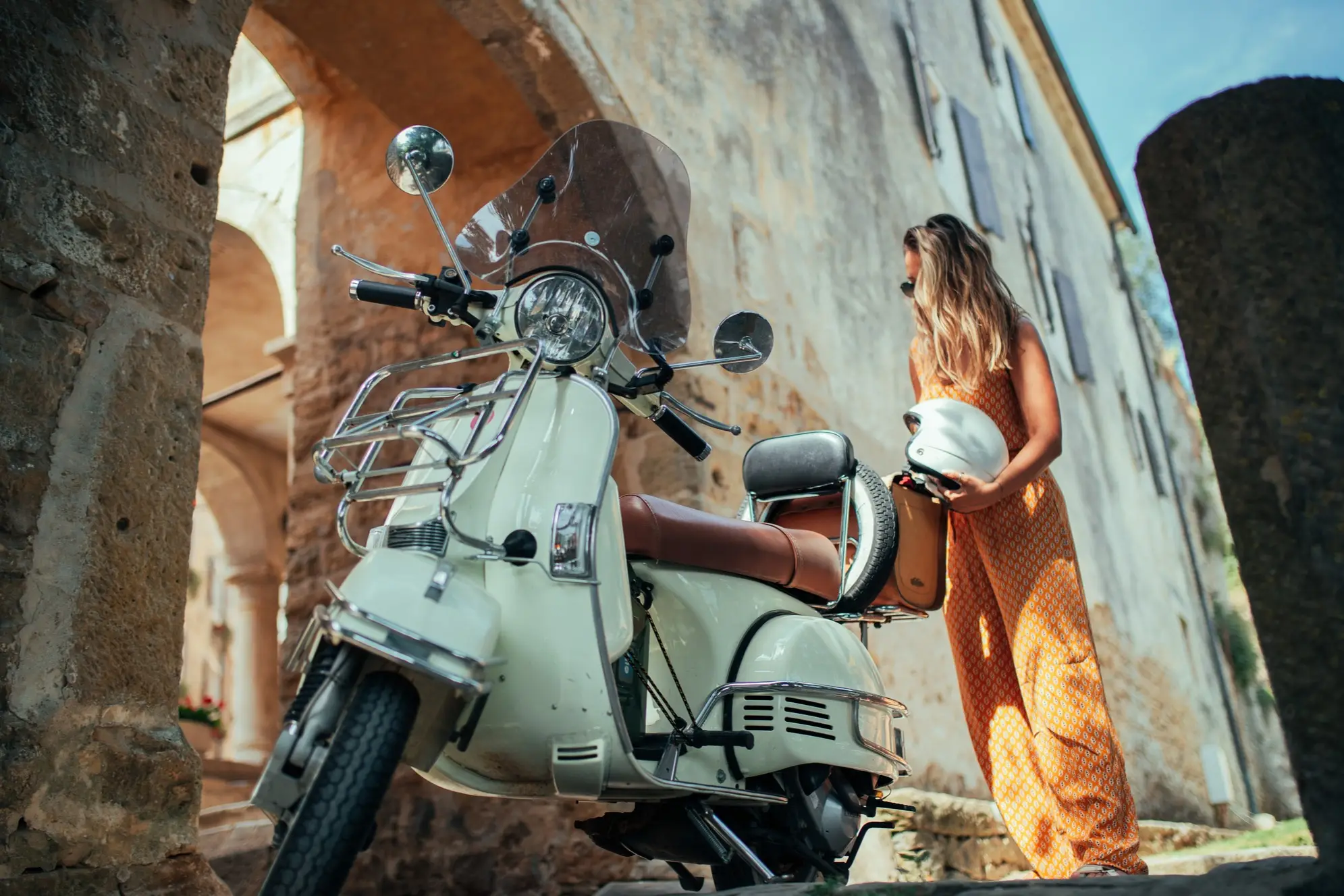 Vespa devant un mur historique et une femme avec un casque à la main