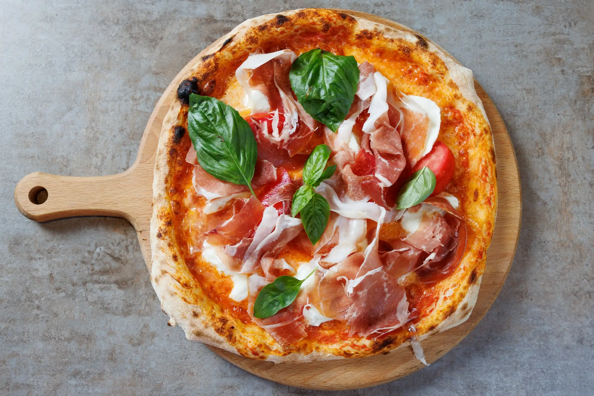 Italien, Essen, Pizza Pizza garniert mit Prosciutto, Basilikum und Kirschtomaten, Käse und Tomatensauce, serviert auf rundem Holzbrett