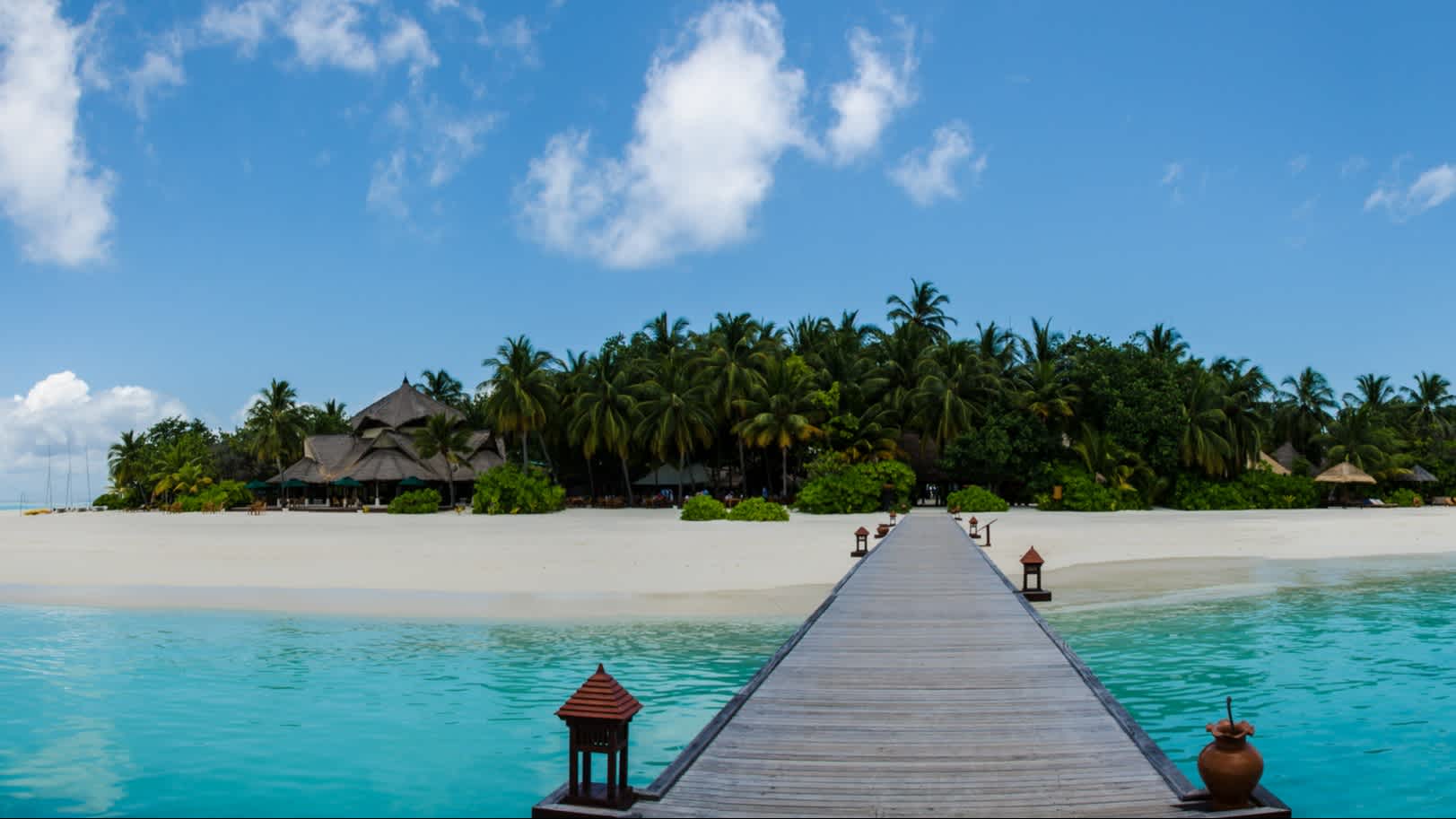 Passerelle en bois menant à une île tropicale avec une plage de sable blanc