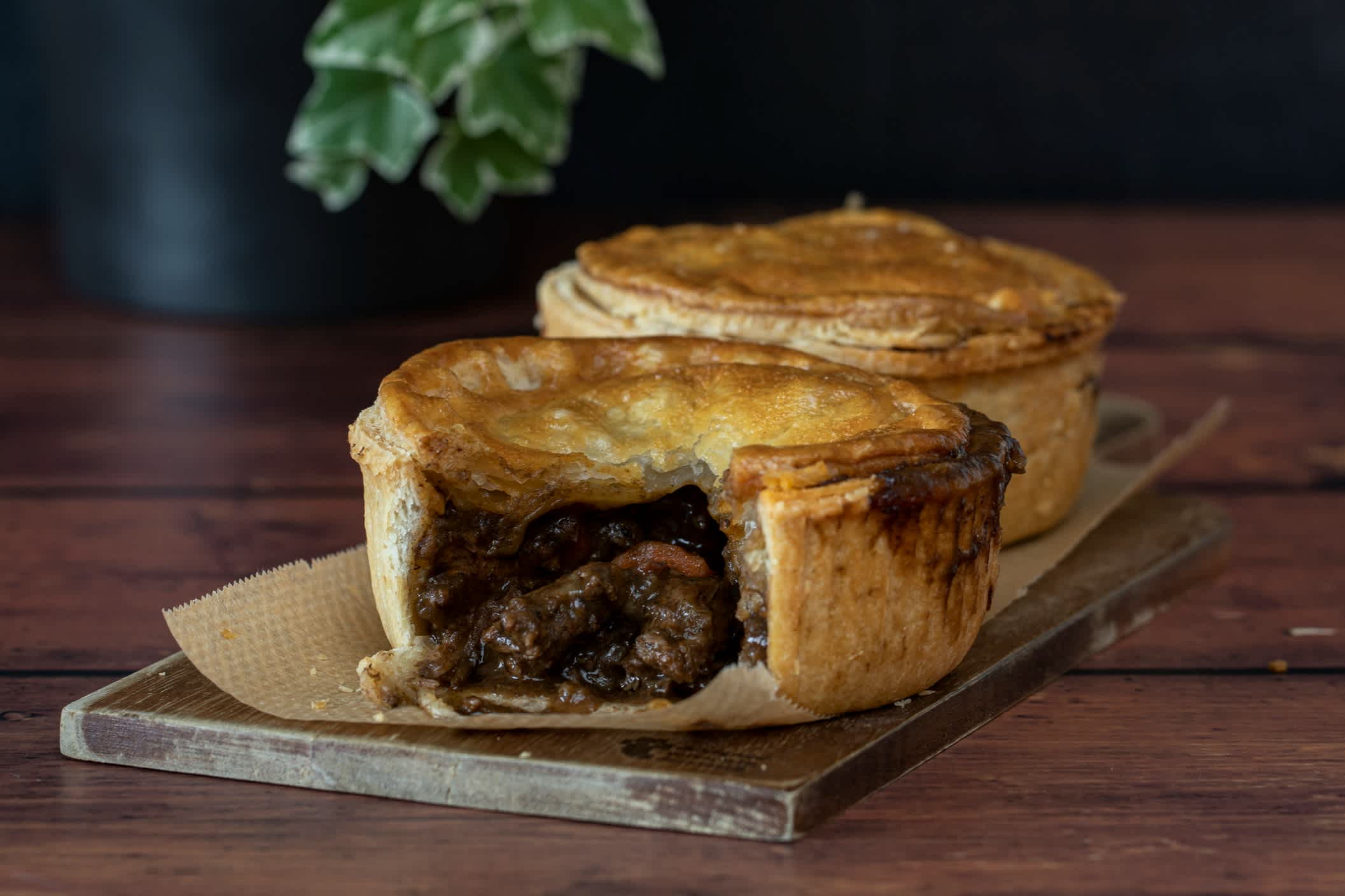 Fleisch- oder Rindfleischkuchen auf Holzbrett, Holztisch und Pflanze im Hintergrund