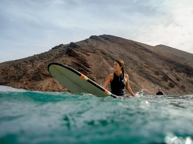 Spanien, Fuerteventura, Corralejo Surferin im Wasser mit Blick auf Berglandschaft. Corralejo, Fuerteventura, Spanien.