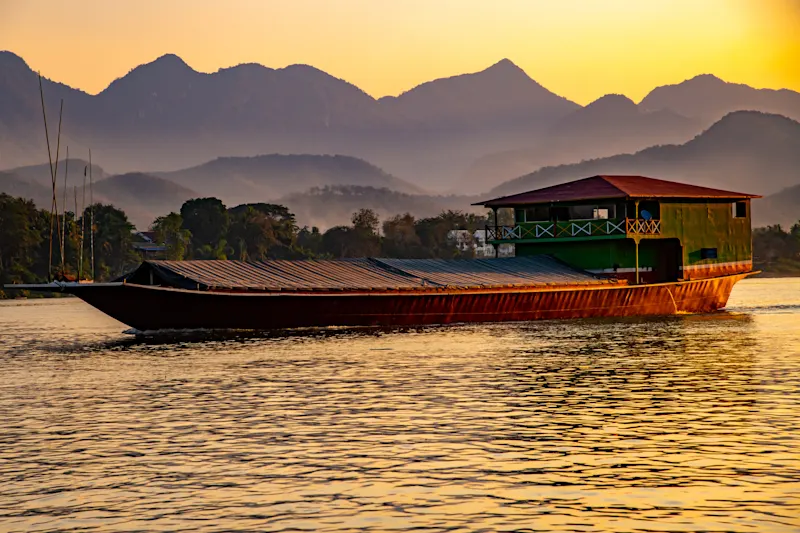 Mékong, coucher du soleil, Laos Bateau traditionnel sur rivière dorée du Mékong au coucher du soleil, et montagnes brumeuses en arrière-plan, Laos.