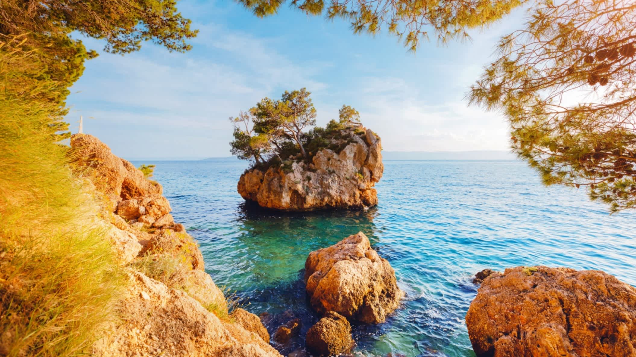 Der Strand von Brela (Punta Rata), Kroatien mit Blick durch Felsen auf einen großen Felsen im Wasser.