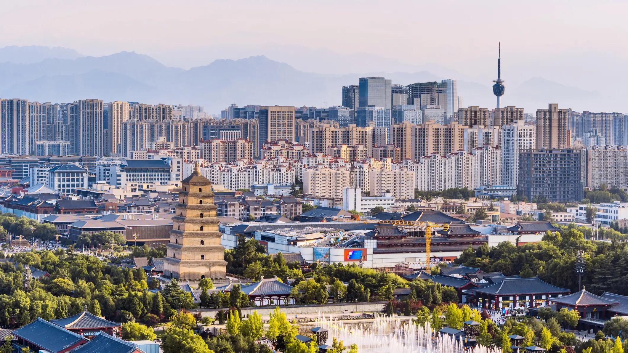 Stadtansicht von Xi'an mit historischer Pagode im Vordergrund, modernen Hochhäusern und Bergen im Hintergrund.