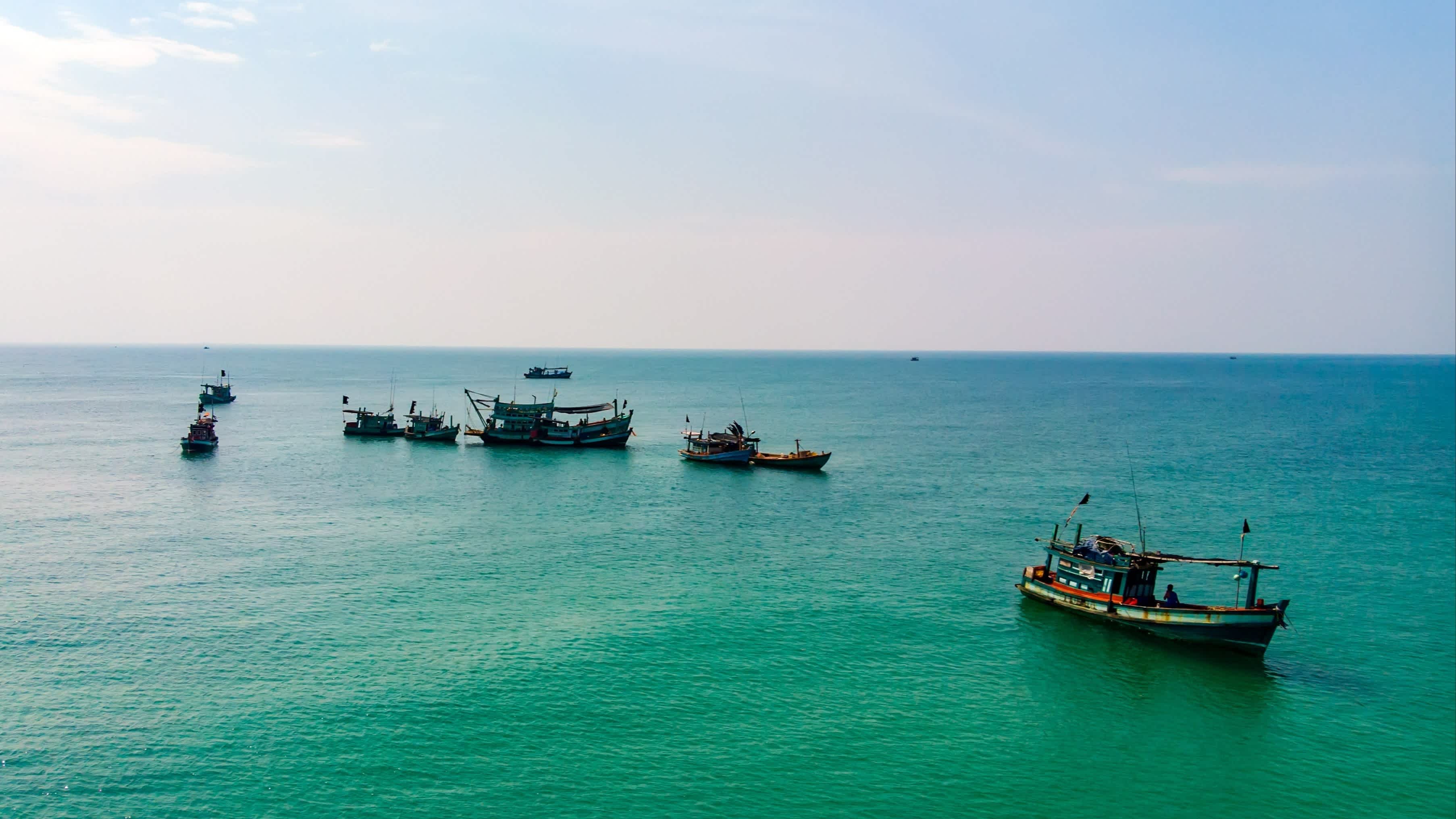 Kleine Fischerboote aus Holz am Strand von Ochheuteal, Kambodscha mit Blick auf das blau-grüne Meer.
