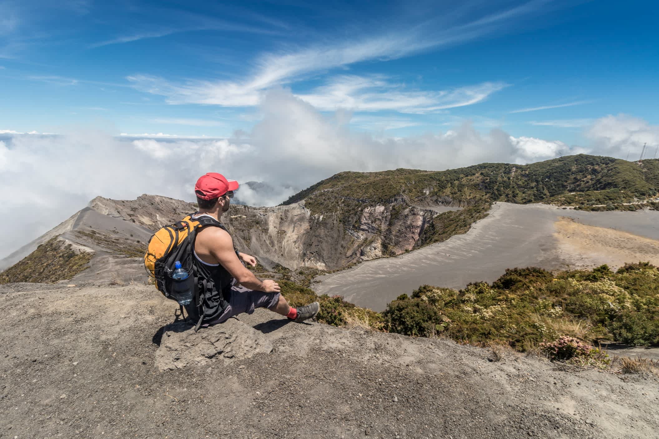 Tourist mit Rucksack sitzt und beobachtet den Hauptkrater im Irazu Volcano National Park in Costa Rica