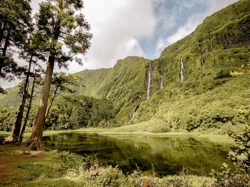 Wasserfall an einer grünen Klippe mit einem ruhigen See. Fajã Grande, Azoren, Portugal.
