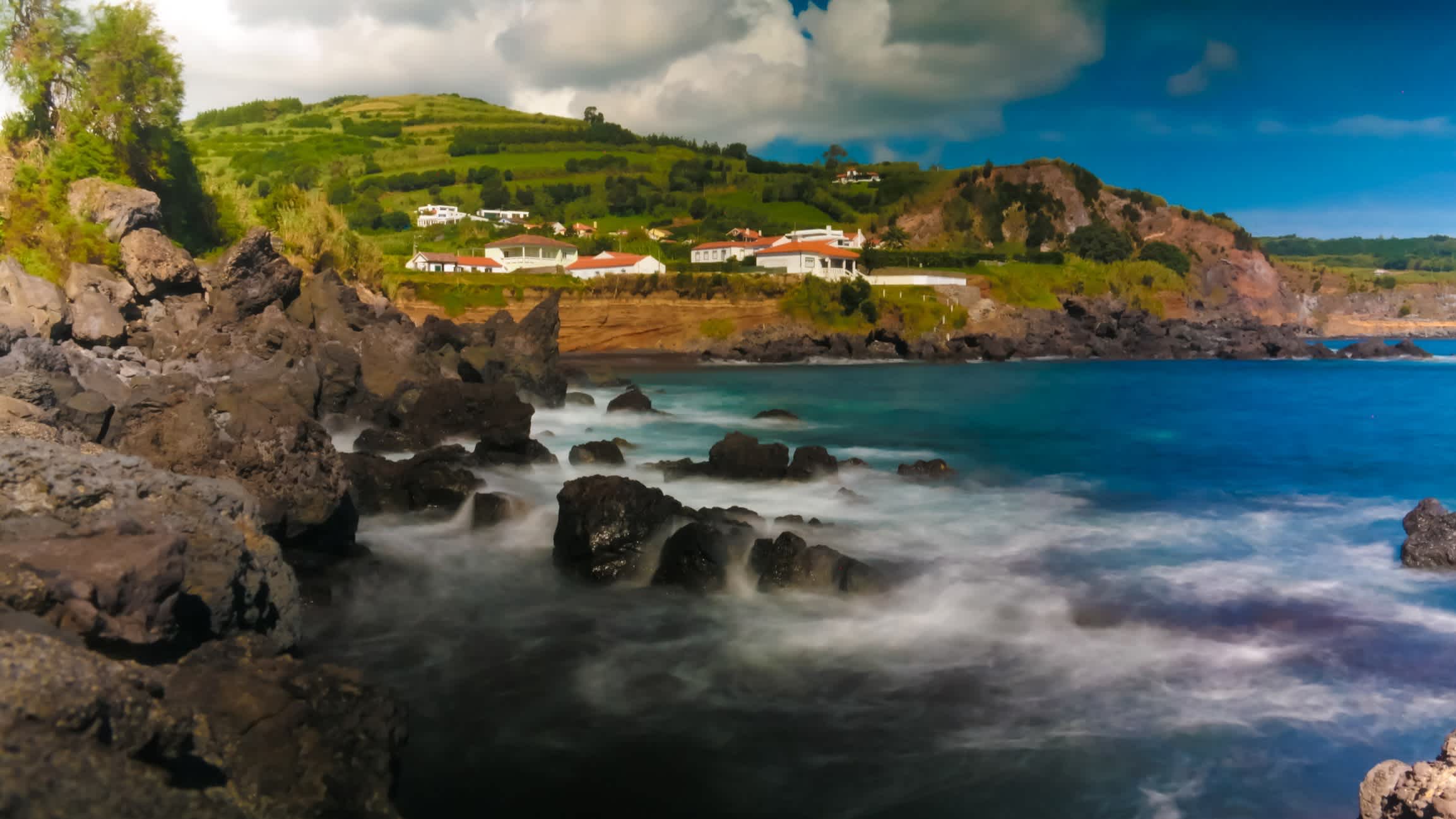 Landschaft der Praia Almoxarife, Faial Insel, Azoren, Portugal mit Blick auf grüne Hügel, Häuser sowie das nebelige Meer.