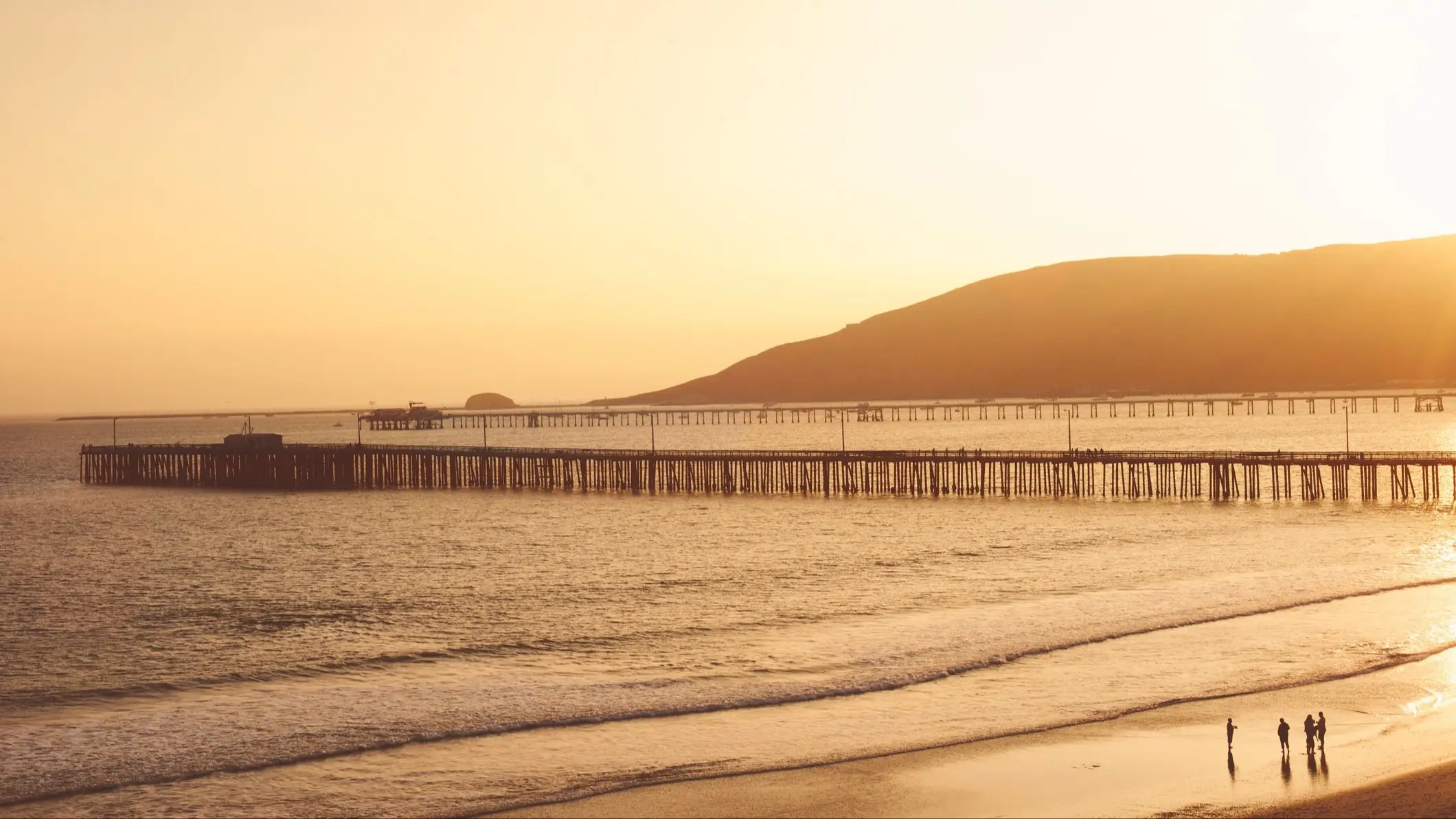 USA Kalifornien Avila Beach Der Strand Avila Beach, San Luis Obispo County Kalifornien, USA bei herrliche orangener Dämmerung und mit Blick auf das Meer, Stege sowie mit Menschen, die am Strand spazieren.