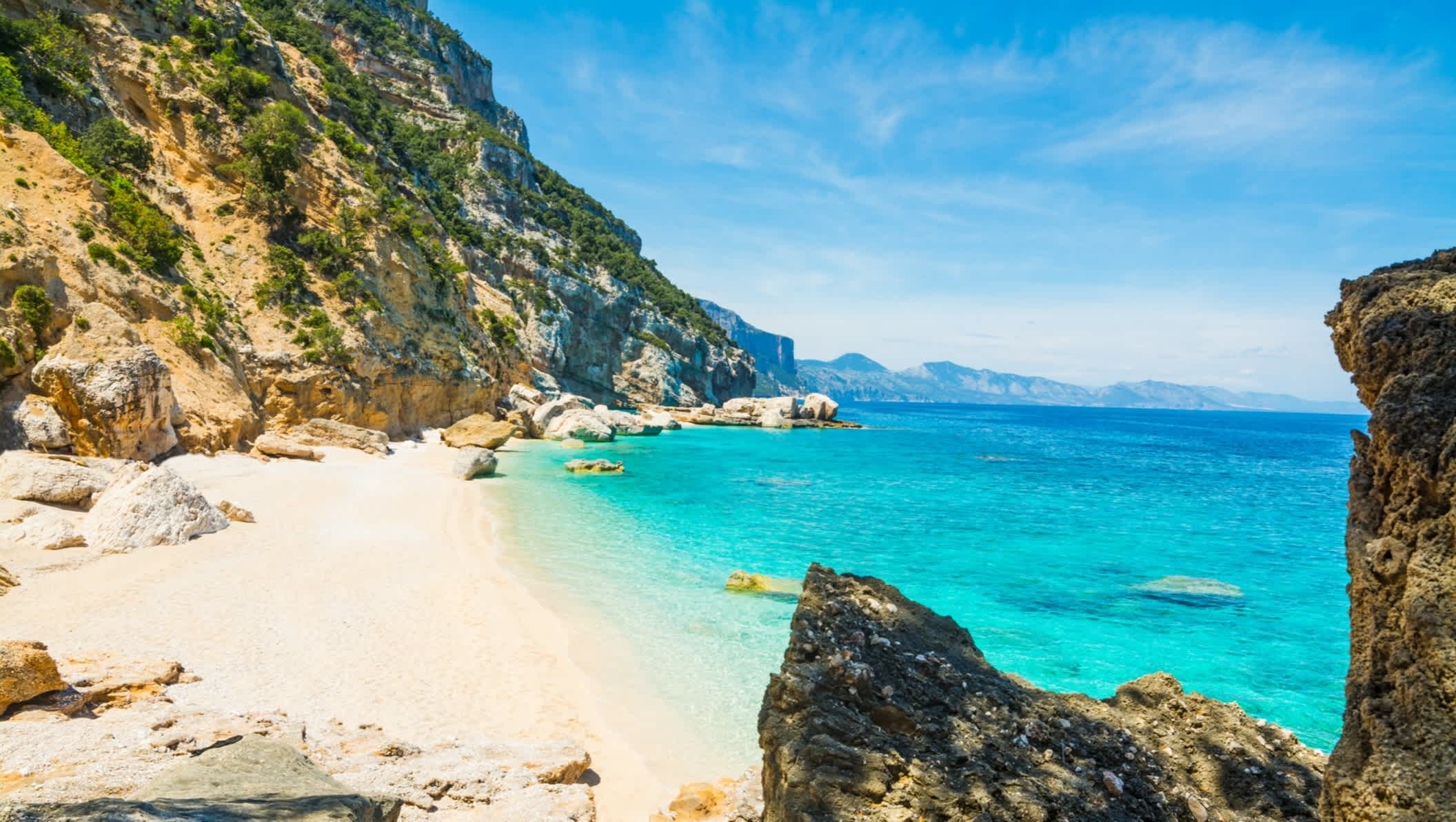 Crique de sable blanc bordée par des rochers verdoyants et une mer turquoise, à Cala Mariolu, en Sardaigne, en Italie.

