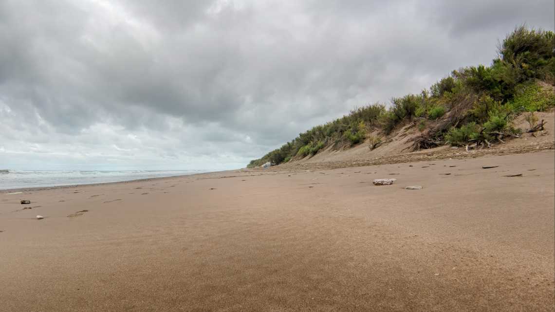 einsamer Strand Sanddünen Vegetation grauer Himmel Wolken Meer
