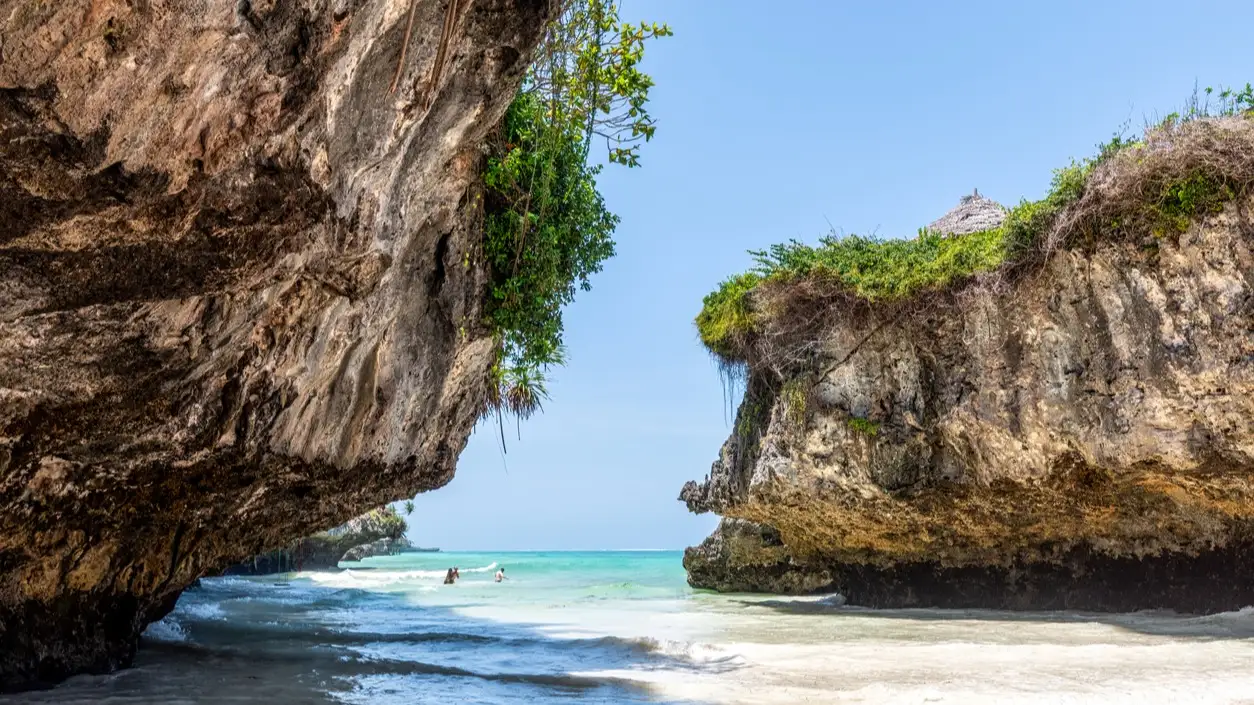 Panorama à couper le souffle de la plage de Mtende à Zanzibar, où l'on voit des baigneurs profiter des eaux turquoise cristallines, le long de la côte rocheuse et au milieu d'un paysage tropical verdoyant