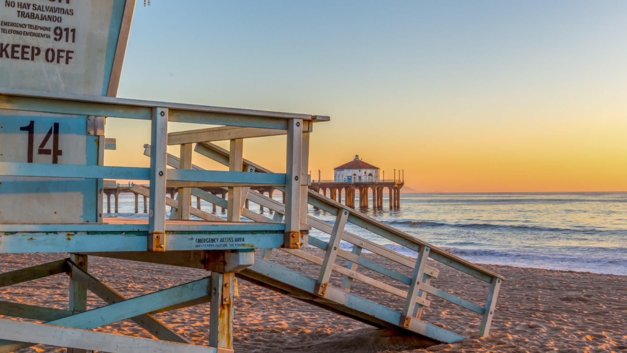 Der Strand Hermosa Beach in den USA, Kalifornien bei Sonnendämmerung und mit dem Meer, einem Wachturm aus Holz sowie einem Steg im Bild.