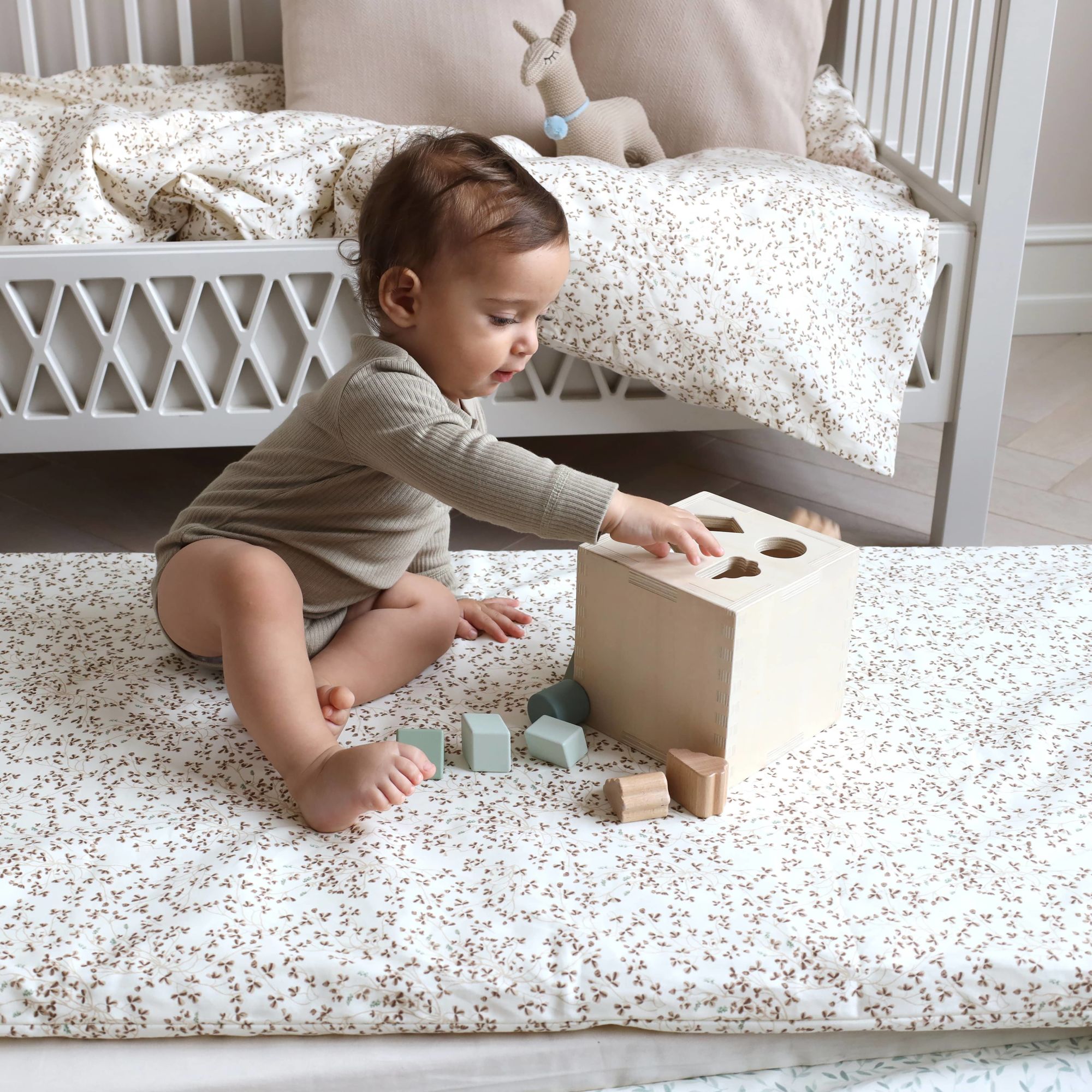 Baby sitting on a nice flower print duvet and playing with his wood toys 