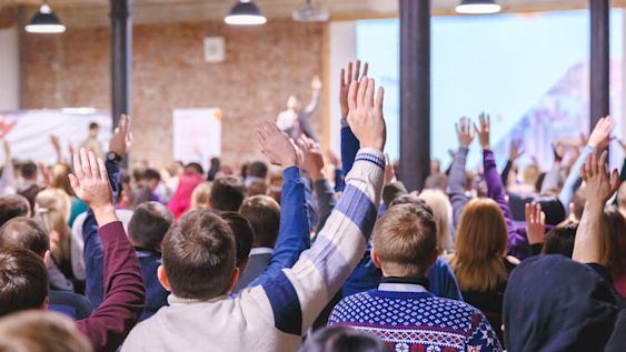 School pupils in an assembly with their hands up.