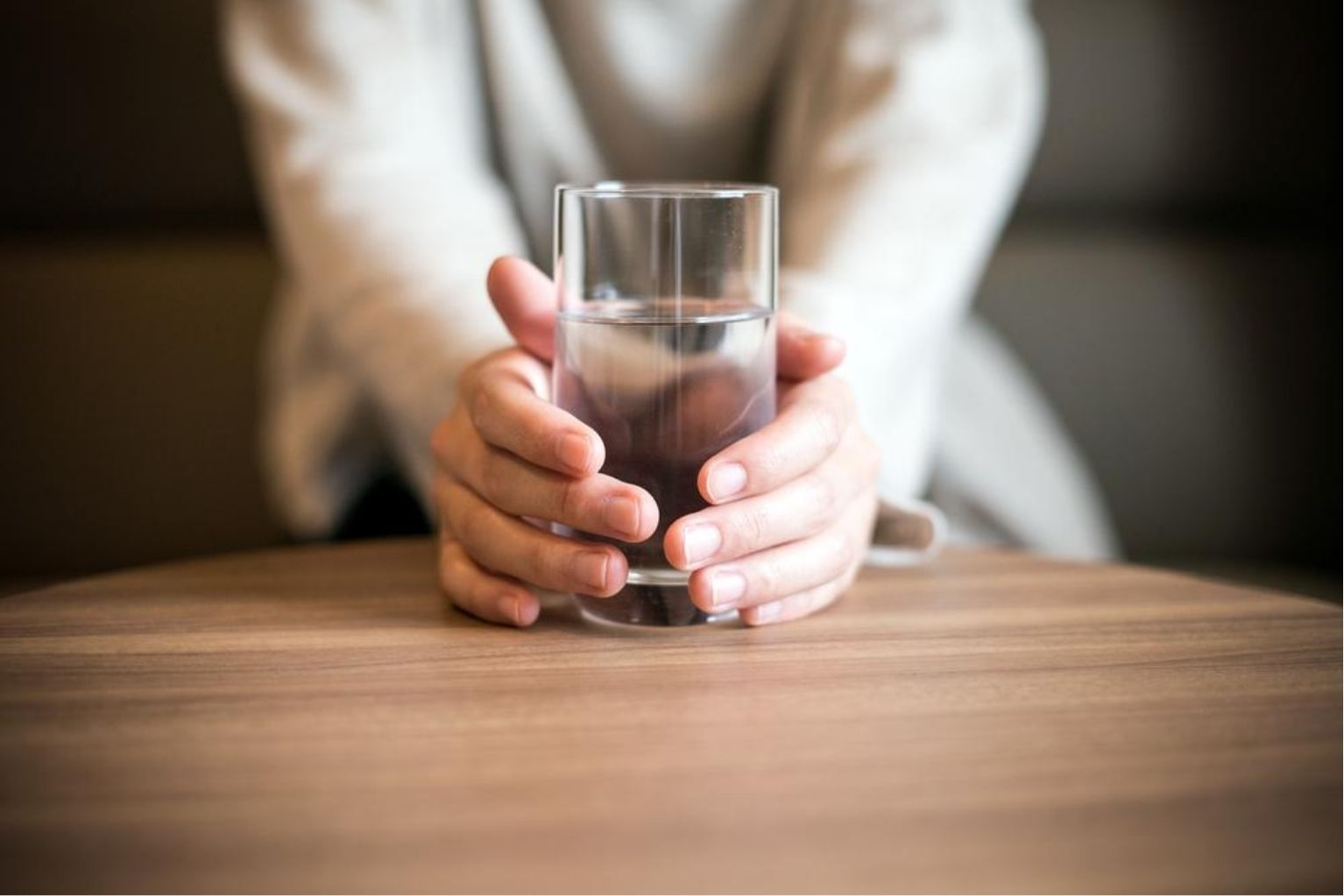 Woman sitting at a table holding a clear glass filled with water