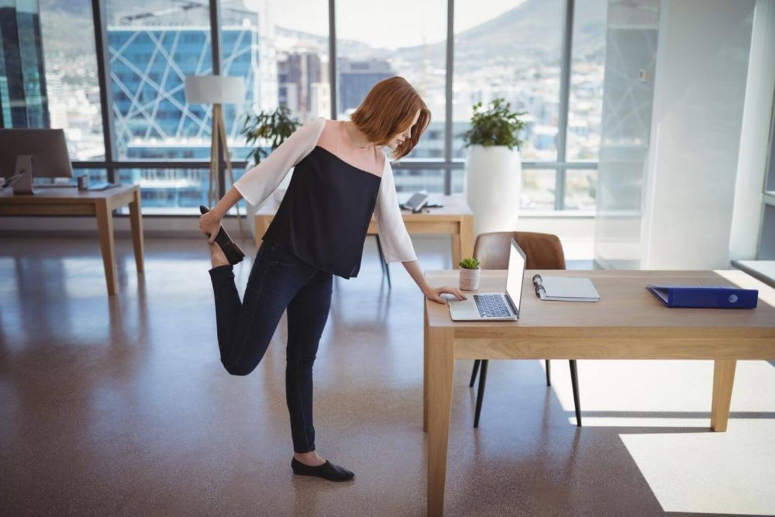 Woman standing at her computer stretching her leg