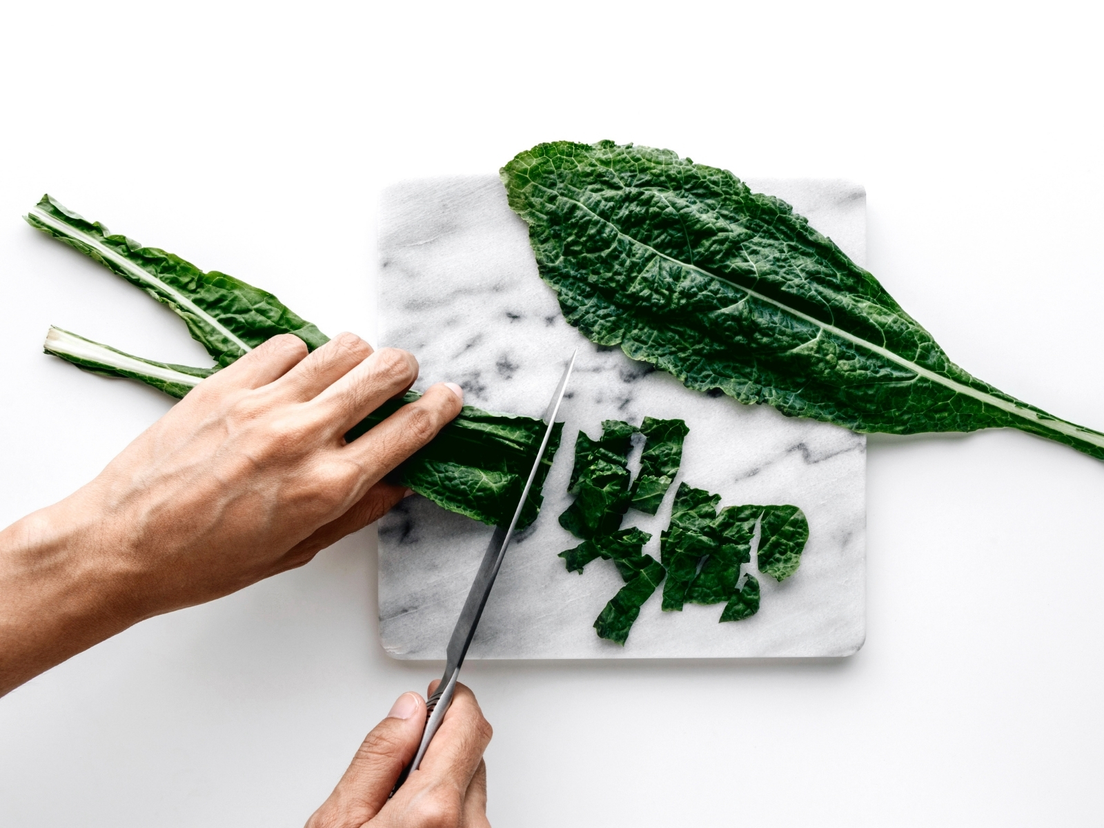 man's hands chopping kale on a marble cutting board
