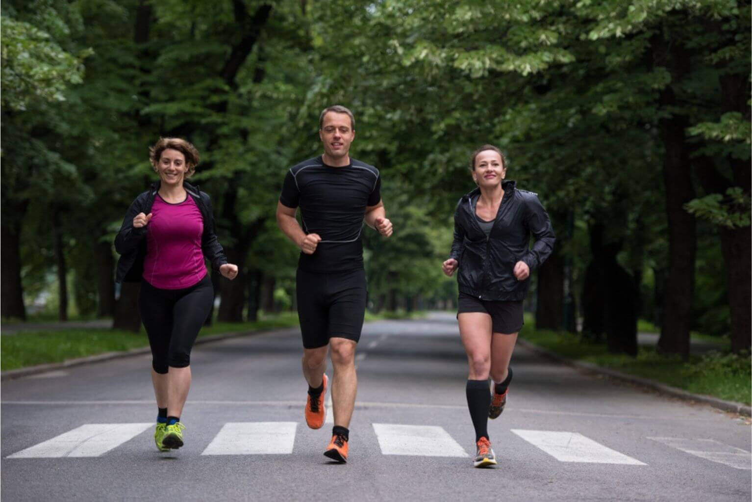 Three people running outside on a road next to trees.
