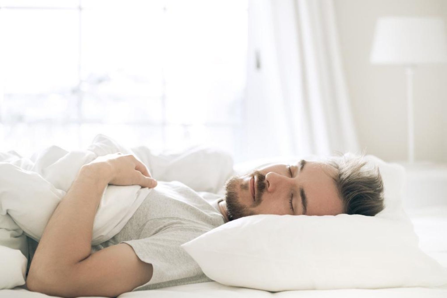 Man sleeping in a bed with white sheets and white pillows