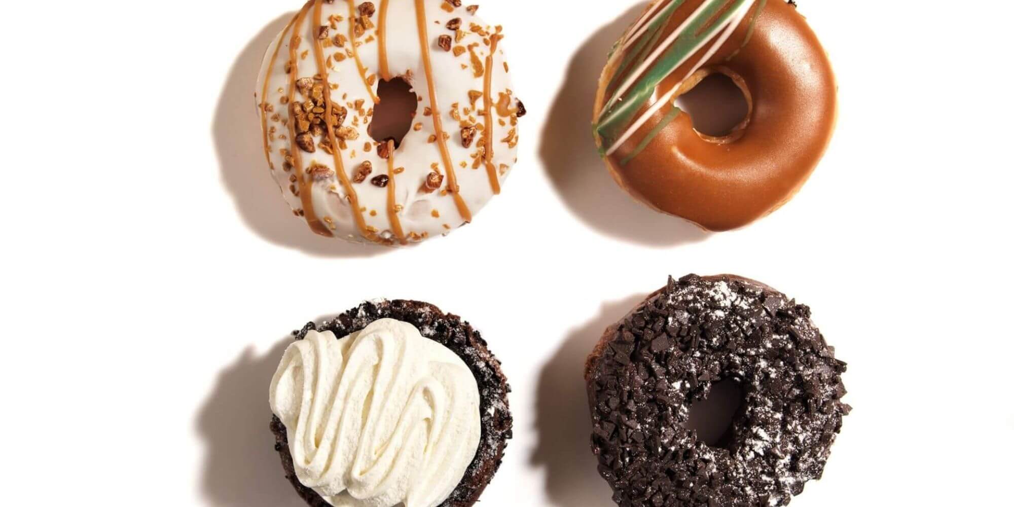 Four doughnuts laying next to each other against a white background all with different toppings.