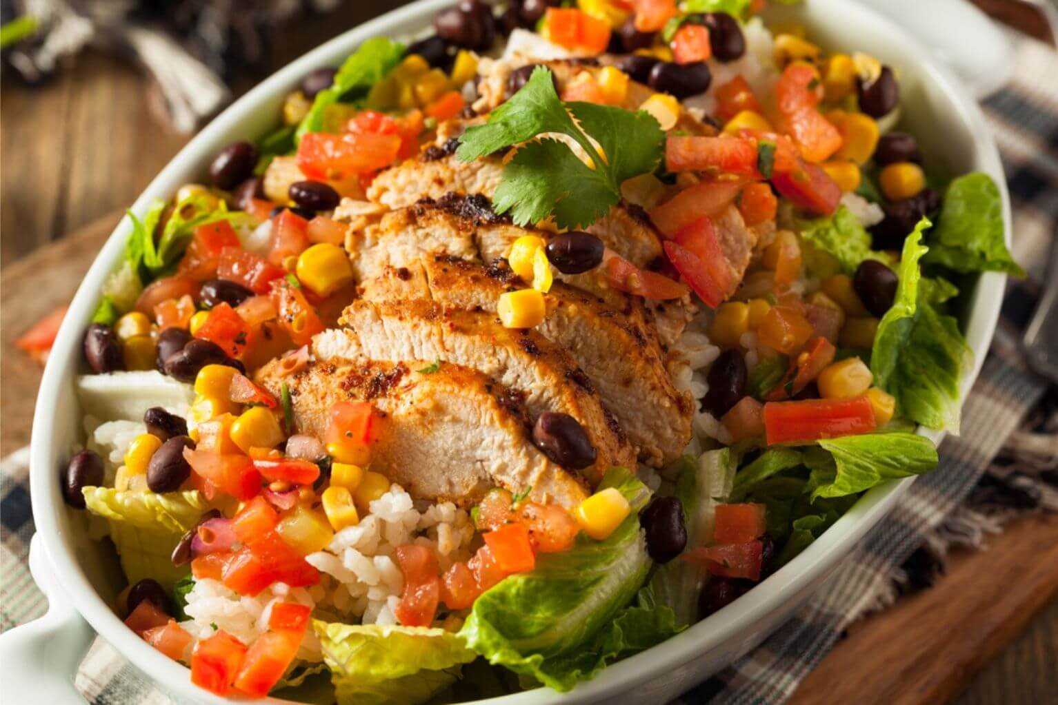 Aerial view of a burrito bowl from Chipotle with chicken, tomatoes, lettuce, black beans, and cilantro.